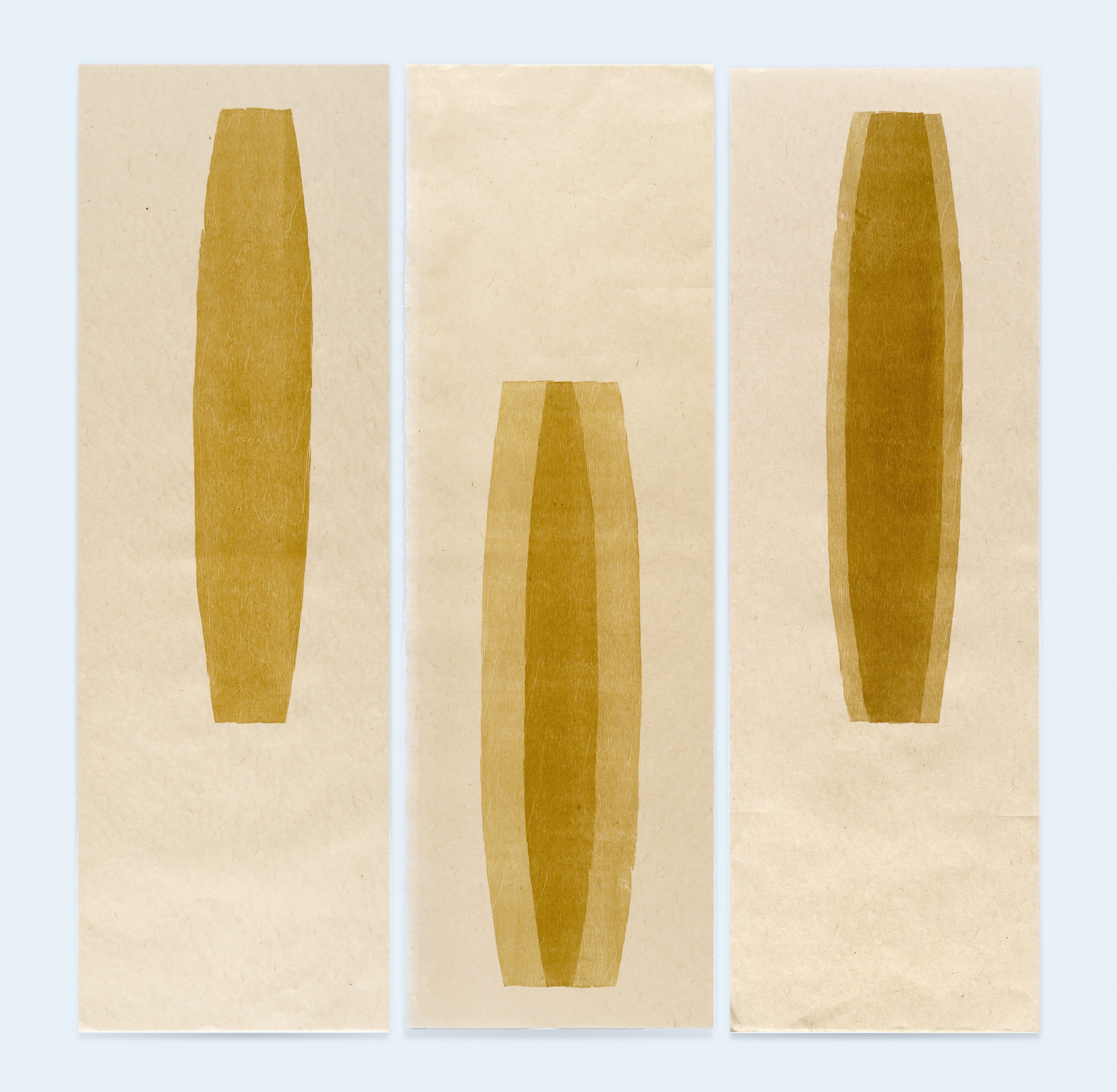 Three vertical panels featuring golden-brown elongated oval shapes on cream-colored paper. The left and right panels display similar narrow forms with subtle shading, while the center panel shows a wider, more tapered oval with deeper tonal variations creating dimensional depth.
