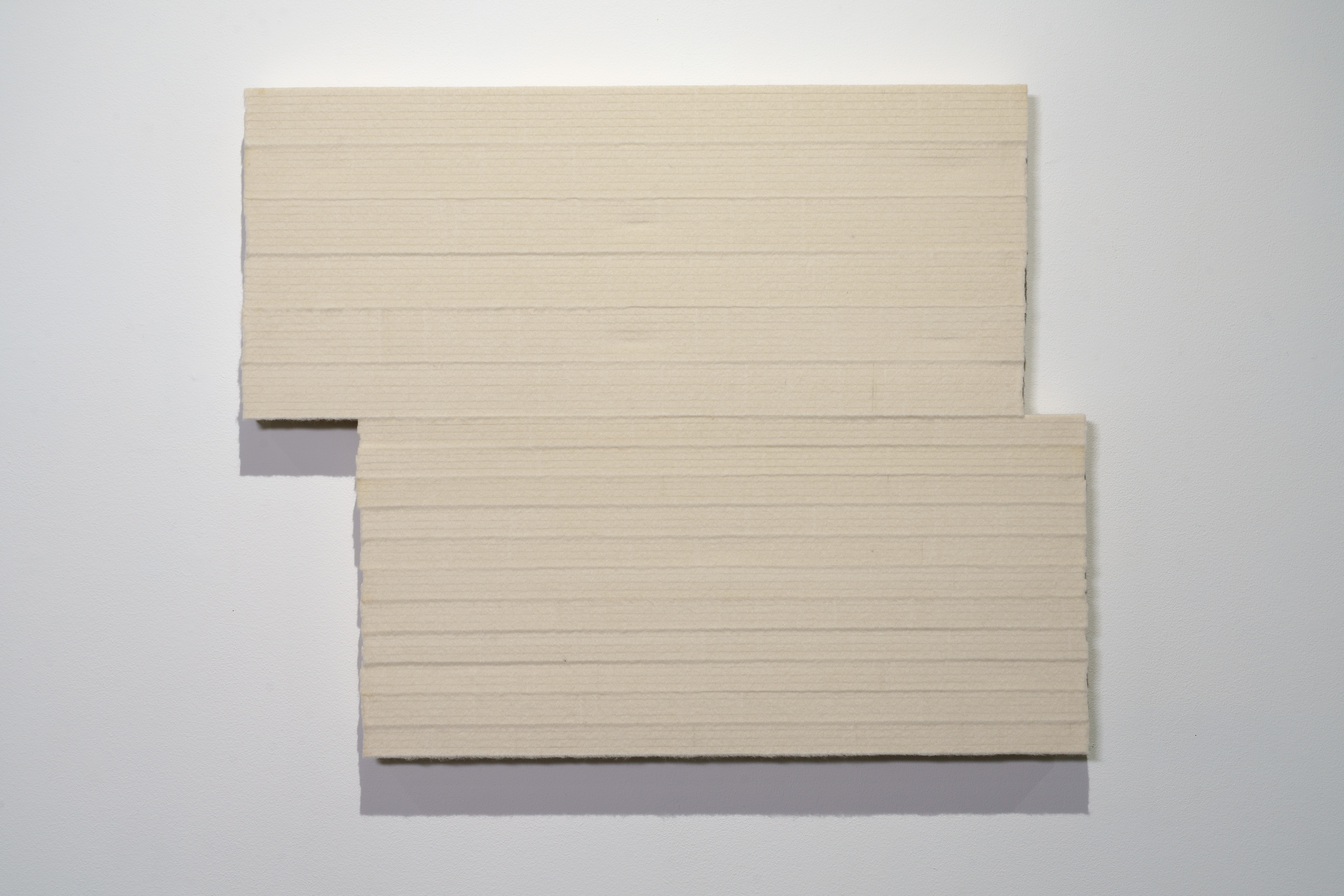 Two rectangular panels of cream-colored textured material arranged in a stepped, offset configuration against a white wall, casting subtle shadows that emphasize their dimensional depth and layered composition.