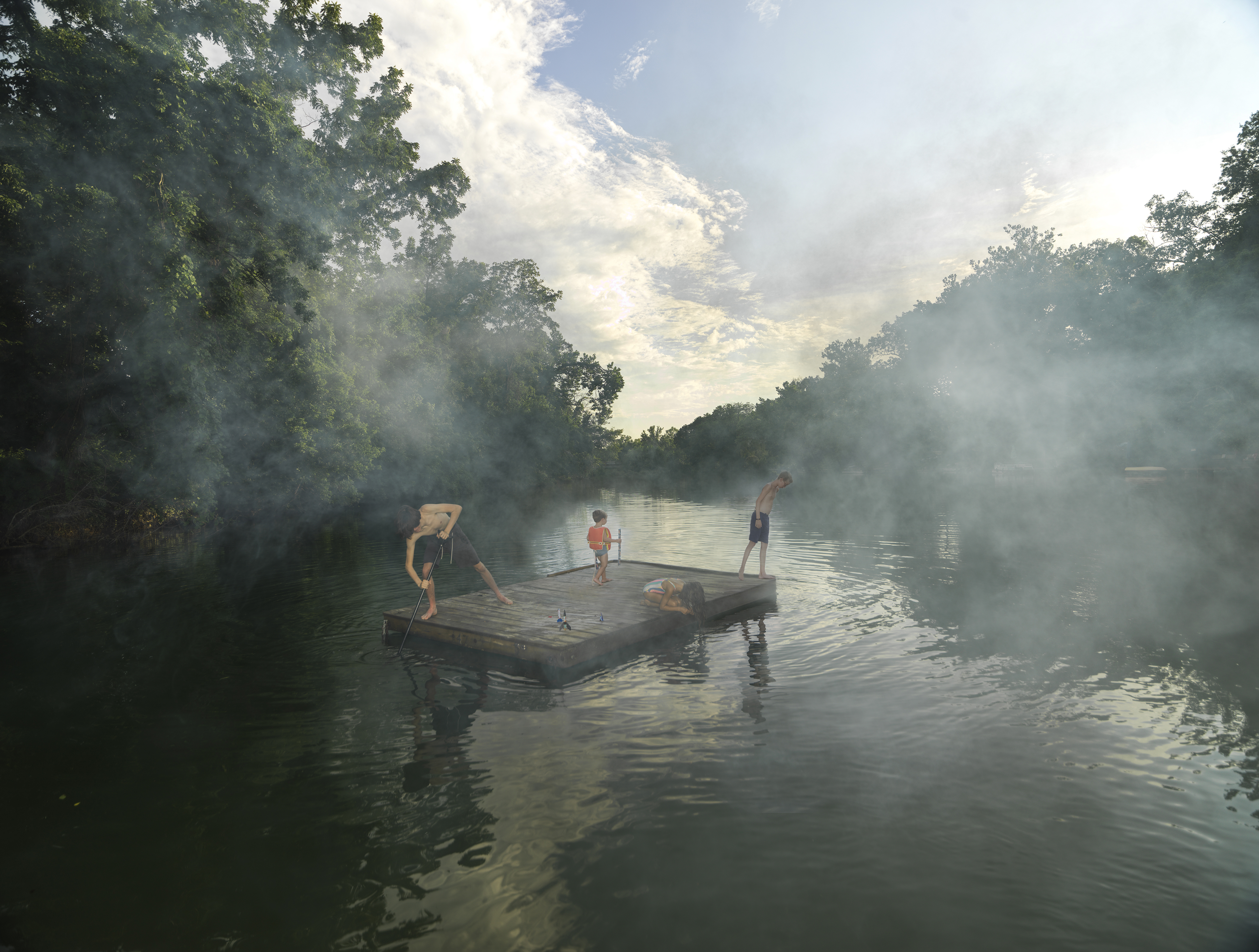 Several figures stand and play on a wooden raft floating in a misty river, surrounded by dense green forest on both banks. Morning or evening light filters through thick fog rising from the water, creating an ethereal atmosphere beneath a clouded sky.