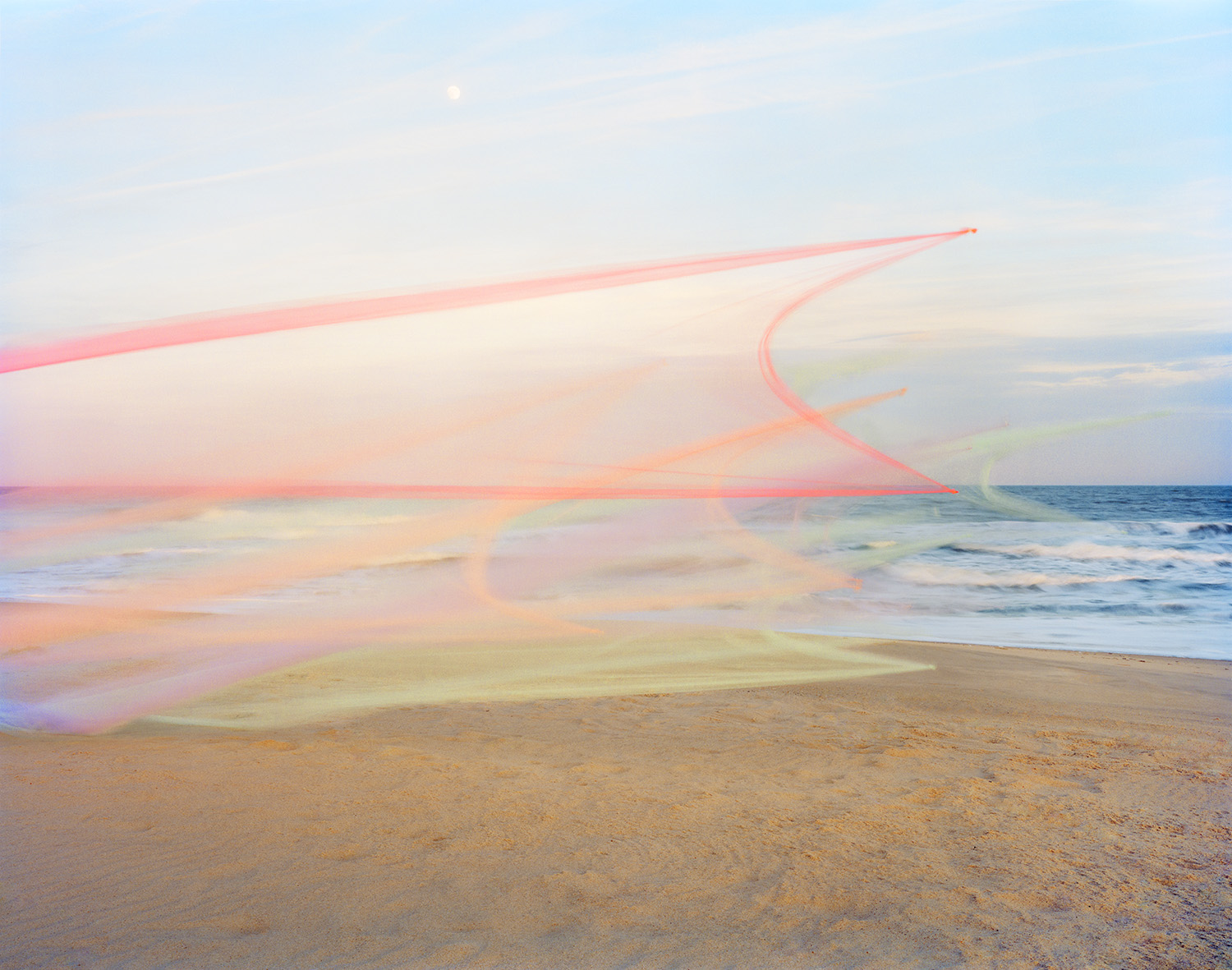 Translucent pink and coral tulle fabric billows across a beach landscape, creating sweeping curved lines that extend from the sand toward the sky. The delicate material overlays the ocean, shoreline, and horizon, blending soft pastel tones of pink, yellow, and green with the natural coastal scenery.