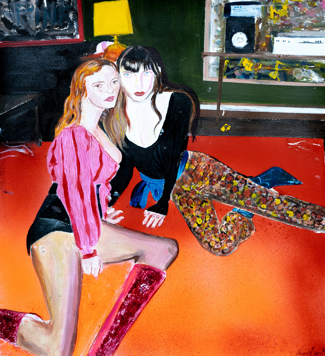 Two stylized female figures with pale skin and bold red lips sit on a vibrant orange-red floor against a dark green wall. The figure on the left wears a pink striped garment with an orange headband, while the figure on the right wears black and blue. Patterned fabric with yellow and earth tones drapes across the composition. The painting employs bold, flat color areas and expressive line work characteristic of contemporary figurative art.