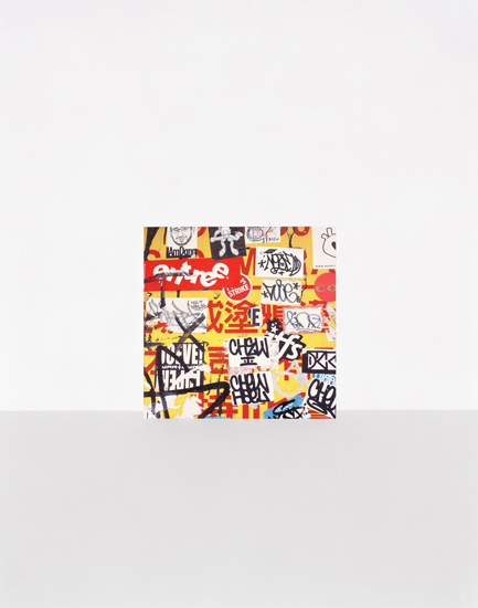 A vibrant collage of overlapping typography and graphic elements featuring bold red, yellow, black, and white colors. Fragmented text and letterforms create a dense, layered composition with a graffiti-like aesthetic, mounted as a print on a neutral gallery wall.