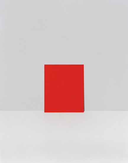 A bright red square positioned centrally against a neutral gray and white background, creating a stark geometric composition with minimal color variation and clean spatial division.
