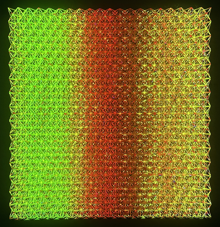 A square grid of repeated geometric patterns in bright neon green, yellow, orange, and deep red, creating a smooth color gradient from cool to warm tones across the composition. The intricate latticed surface has a three-dimensional quality with raised, faceted elements that cast subtle shadows, set against a dark background.