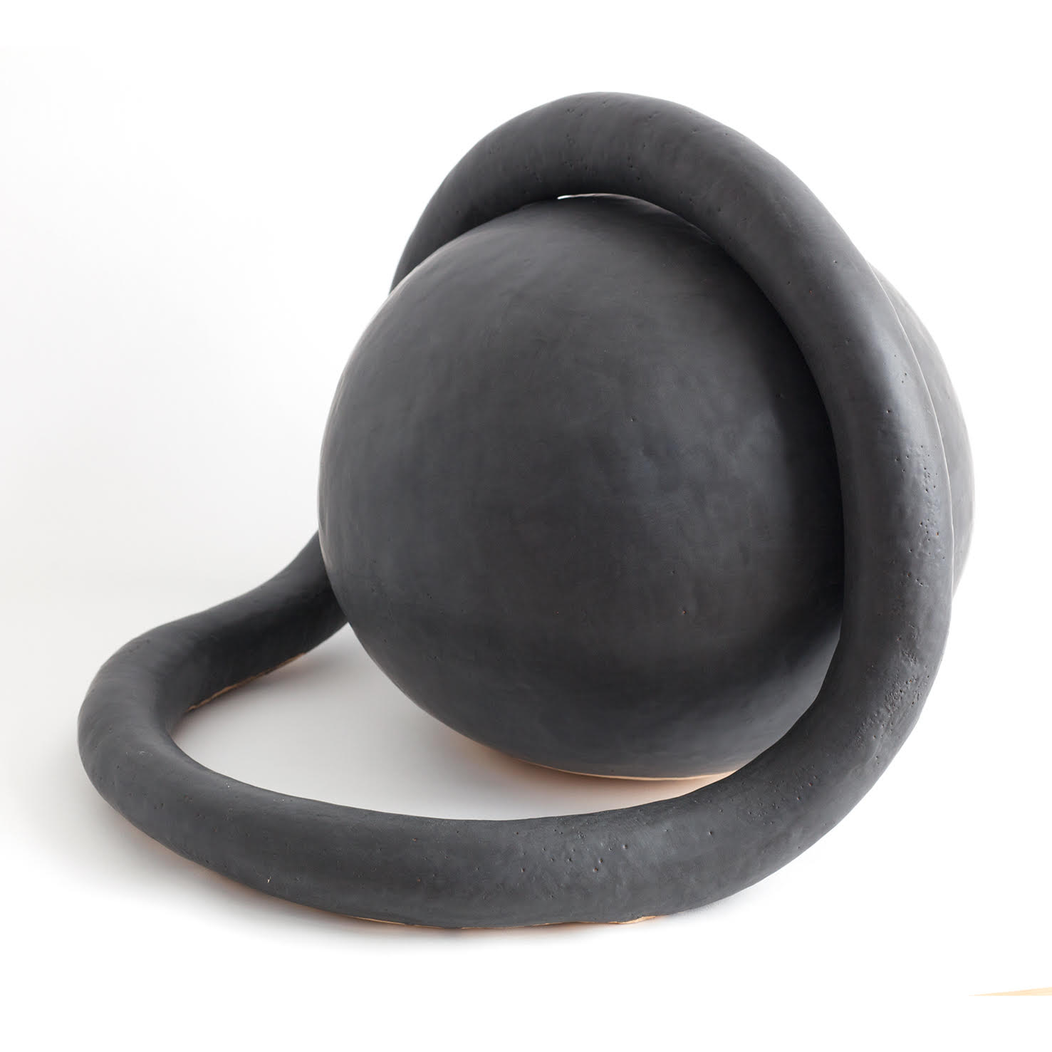 Abstract ceramic sculpture in dark charcoal glaze featuring a curved, organic form with a spherical element perched atop a sweeping, loop-like base, set against a white background.