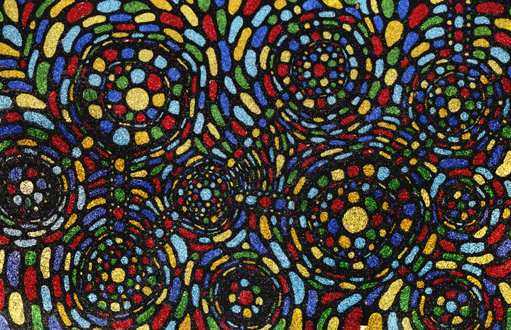 Vibrant abstract composition featuring concentric circular swirls rendered in bold primary colors—red, blue, yellow, and green—with shimmering glitter and textured cut paper creating dynamic movement across the dark background.