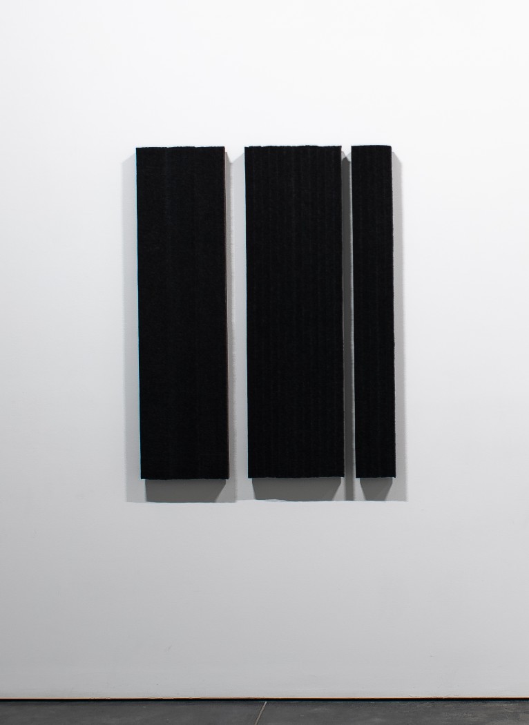 Three vertical rectangular panels of black wool felt mounted on a white gallery wall, with subtle shadows cast beneath each panel creating depth and dimension against the minimalist composition.