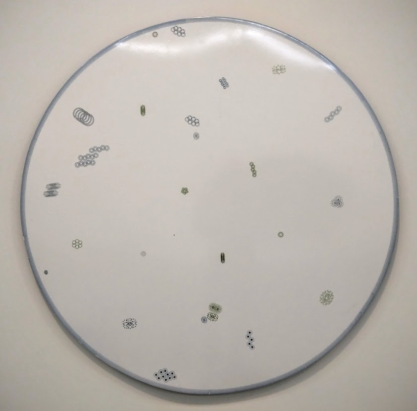 A large circular white panel with a blue-gray border displays scattered small algorithmic drawings in black, green, and gray throughout its surface. The delicate, intricate marks vary in size and pattern, creating an organic, dispersed composition against the pristine white ground.