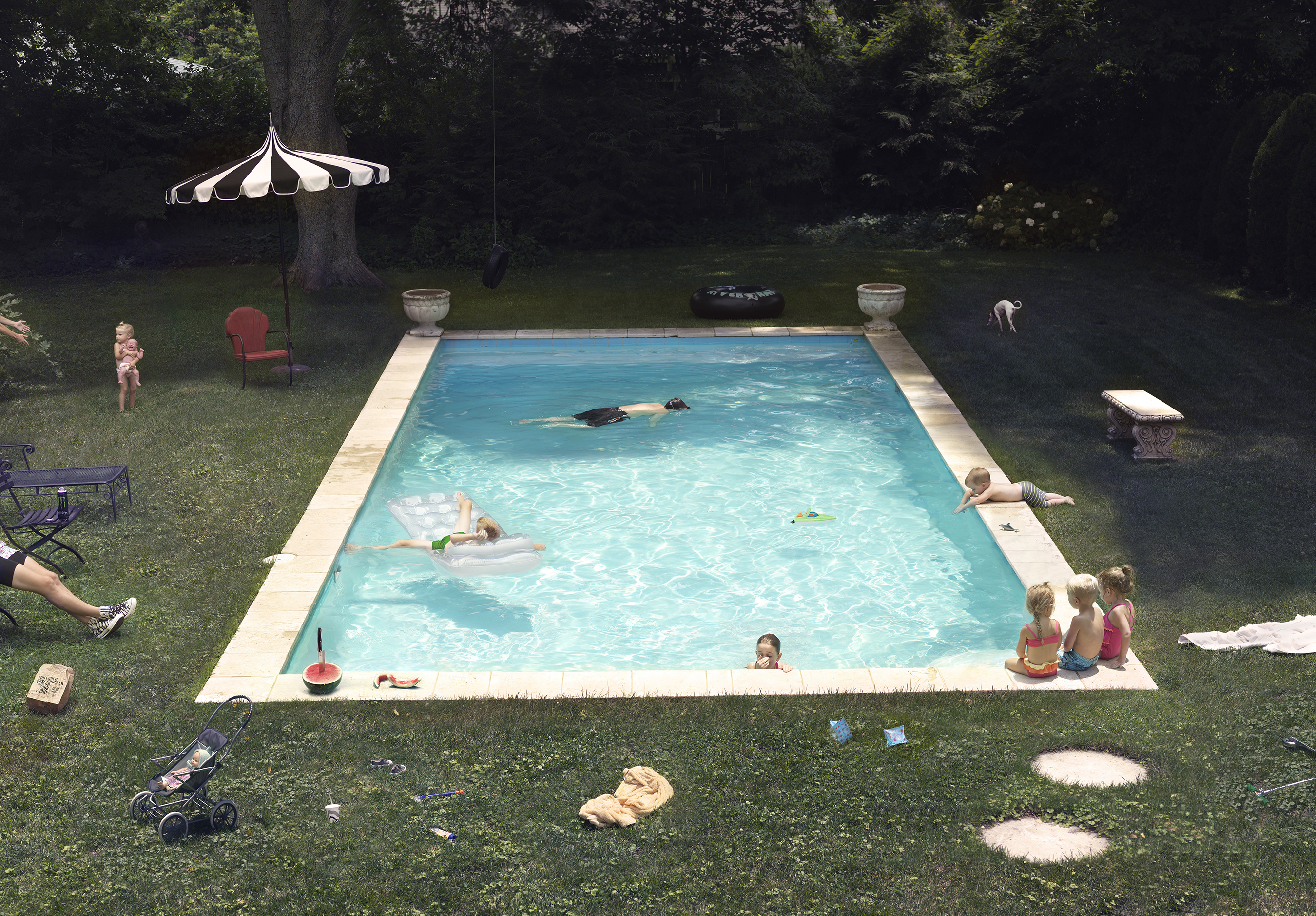 A bright turquoise rectangular swimming pool set in a manicured lawn surrounded by a dense forest, with multiple figures swimming and lounging around its perimeter. A striped black and white umbrella shades a red chair on the left, while various recreational items—floats, toys, a stroller, and picnic supplies—scatter across the grass, creating a leisurely suburban scene rendered in vivid, saturated colors.
