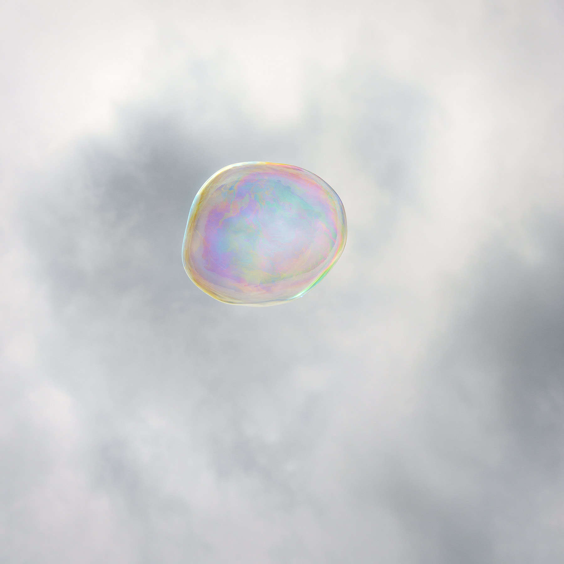 A translucent soap bubble floats against a soft, clouded gray sky. Iridescent pastel hues—pink, blue, yellow, and green—shimmer across its delicate spherical surface, creating an ethereal and luminous effect.