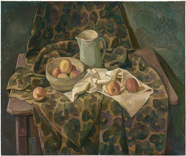 A still life composition featuring a table draped with patterned green and gold fabric, displaying a ceramic pitcher, a bowl of apples, and scattered fruit on white cloth. The muted palette of browns, greens, and ochres creates a harmonious arrangement rendered in a modernist style with simplified forms and bold patterning.