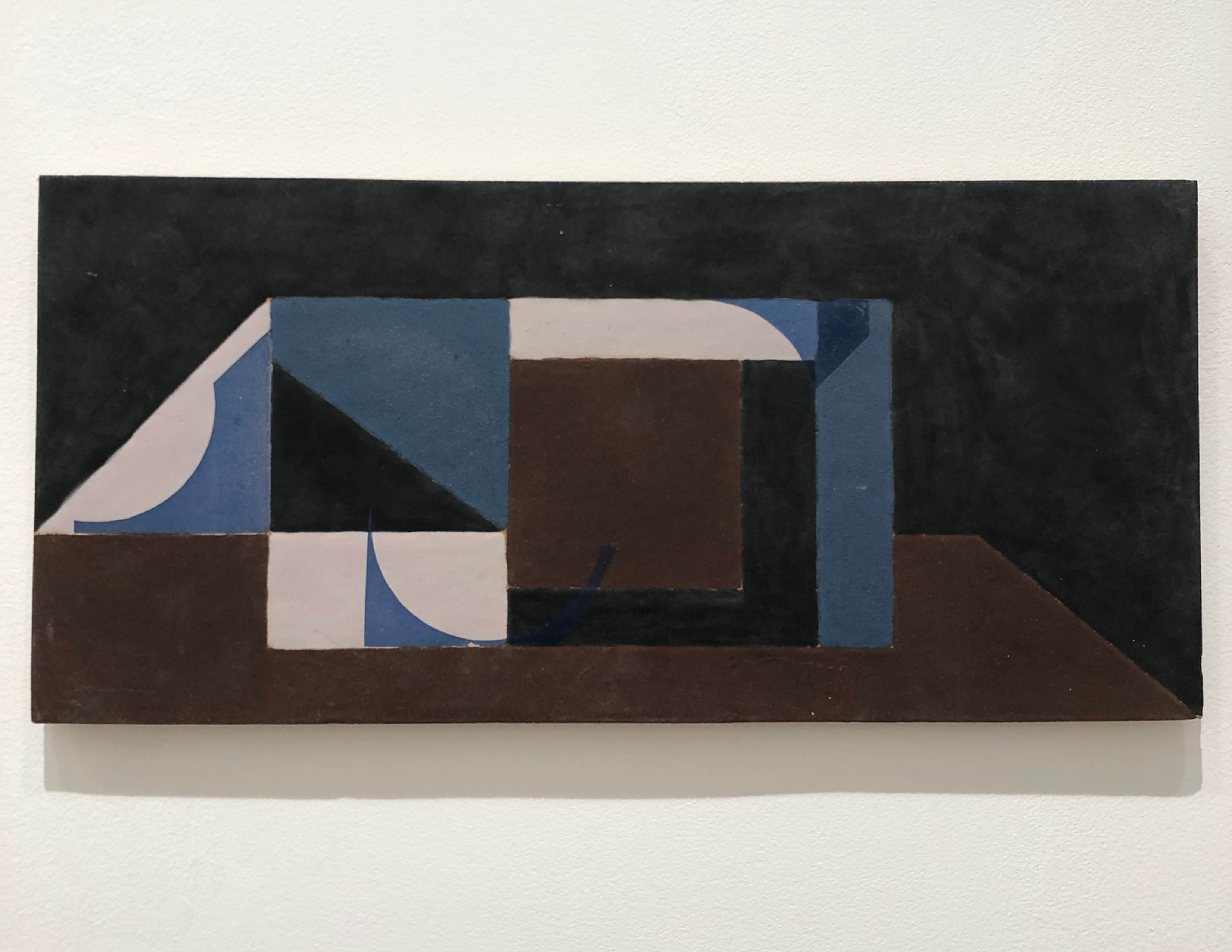 Abstract geometric composition in ceramic featuring interlocking rectangular forms in dark blue, cream, brown, and black with curved elements. The layered, three-dimensional design creates a sense of depth and movement across the horizontal surface.
