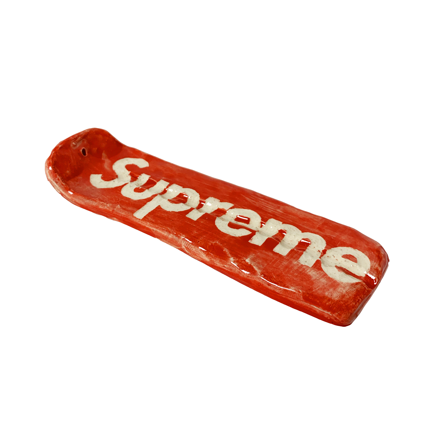 A red ceramic vessel with cream-colored lettering spelling "Supreme" runs along its length. The hand-formed clay piece has an organic, slightly asymmetrical shape with a shallow bowl at one end and tapers toward the opposite end, showing visible brushwork and glaze variations across its surface.