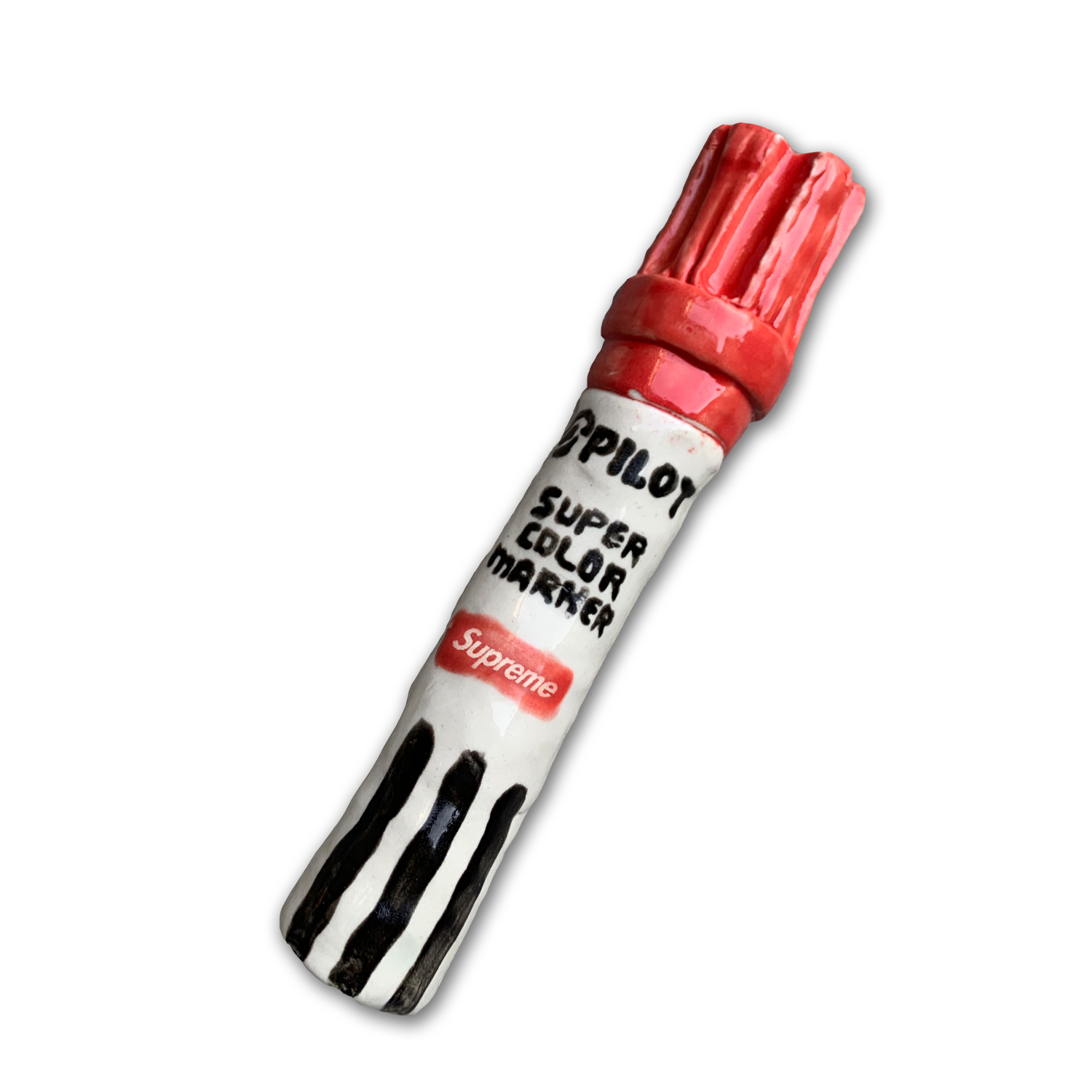 A sculptural marker with a red cap and black stripes rendered in ceramic materials, featuring white label sections with printed text reading "PILOT SUPER COLOR MARKER" and "Supreme." The object mimics the scale and proportions of an actual oversized marker.