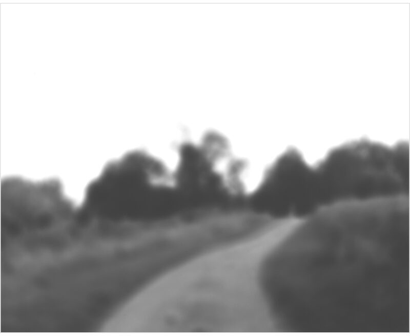 A soft-focus black and white landscape depicting a rural road lined with trees receding into a hazy distance, rendered in subtle gradations of gray with a dreamlike, atmospheric quality.