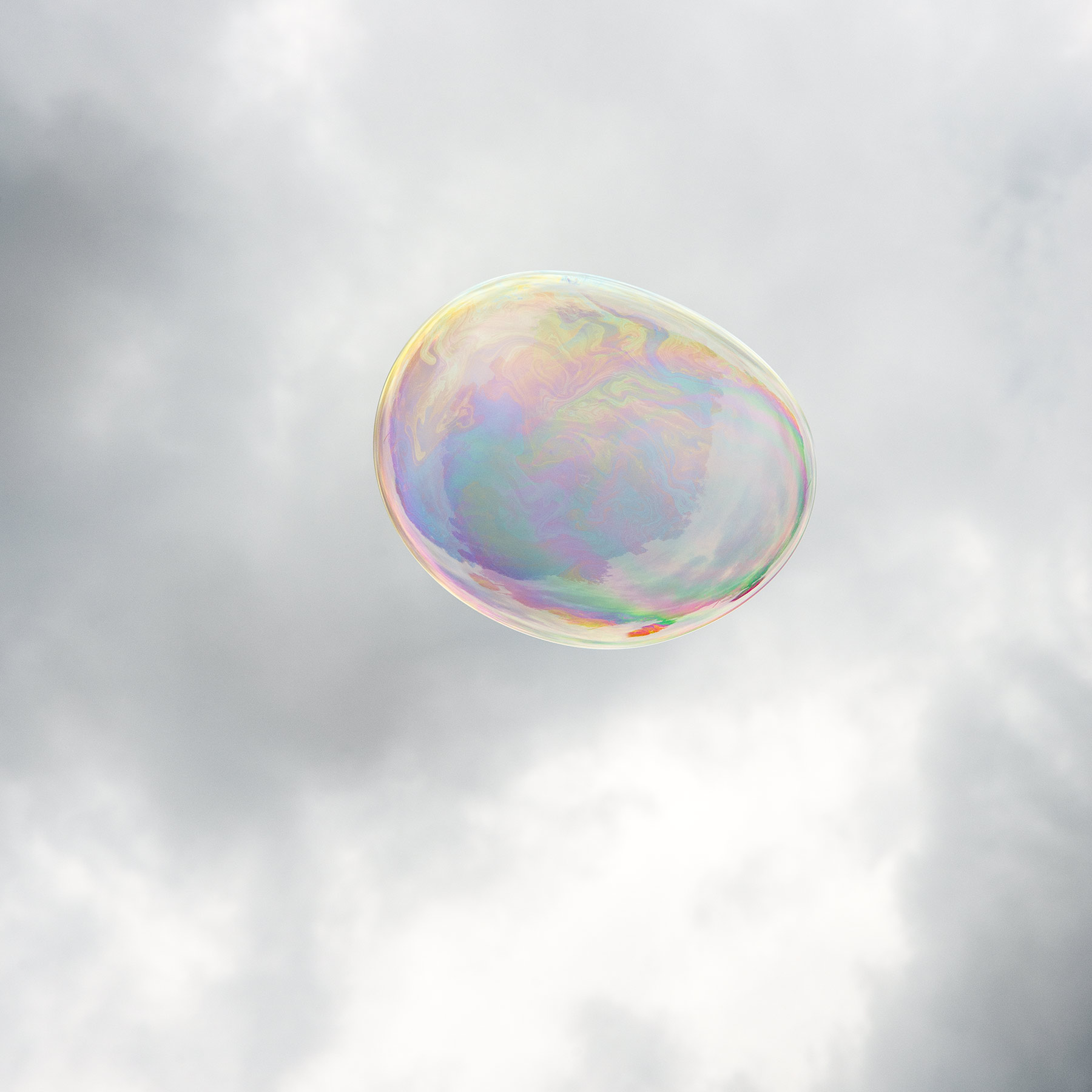 A translucent soap bubble floats against a soft, cloudy sky, its spherical surface shimmering with iridescent bands of pink, purple, blue, and gold that shift across its curved form.