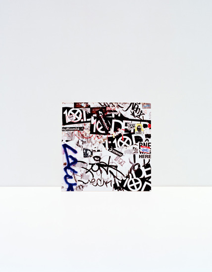 A collage of black and white graphic elements, typography, and street art-style markings overlaid on a light background, featuring fragmented text, geometric shapes, and gestural marks in blue and black ink.