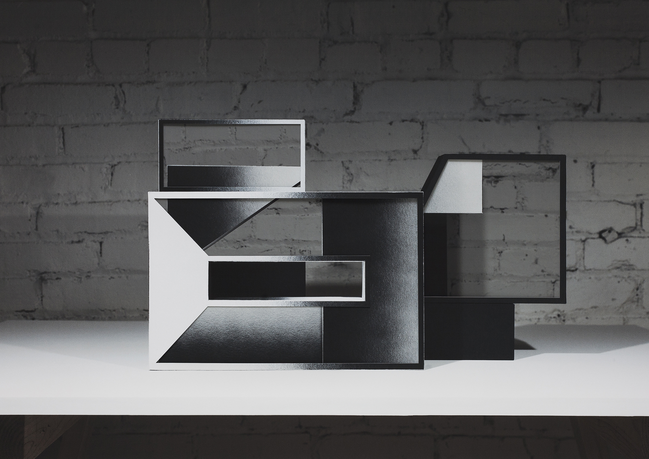 Abstract geometric composition featuring interlocking rectangular frames in black and white, layered to create a three-dimensional effect against a weathered brick wall background. The fragmented, overlapping planes suggest architectural forms with varying depths and contrasting tones.