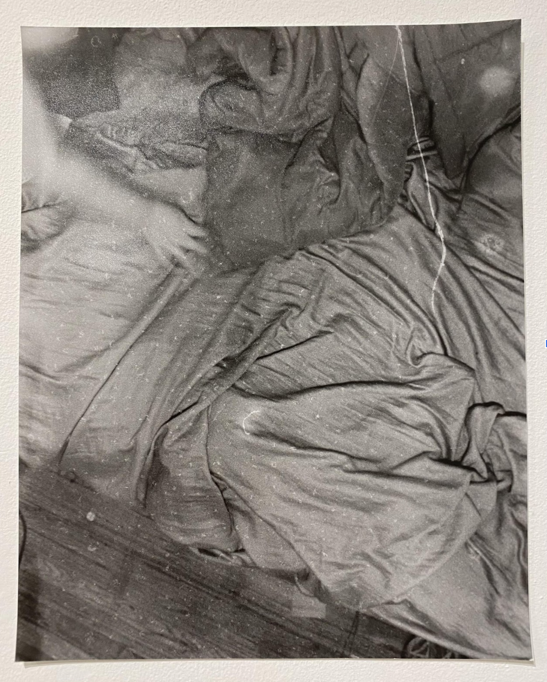 Black and white photograph of crumpled bedsheets and fabric, captured from above. The composition emphasizes the play of light and shadow across deep folds and wrinkles, creating an abstract study of texture and form in the tangled cloth.