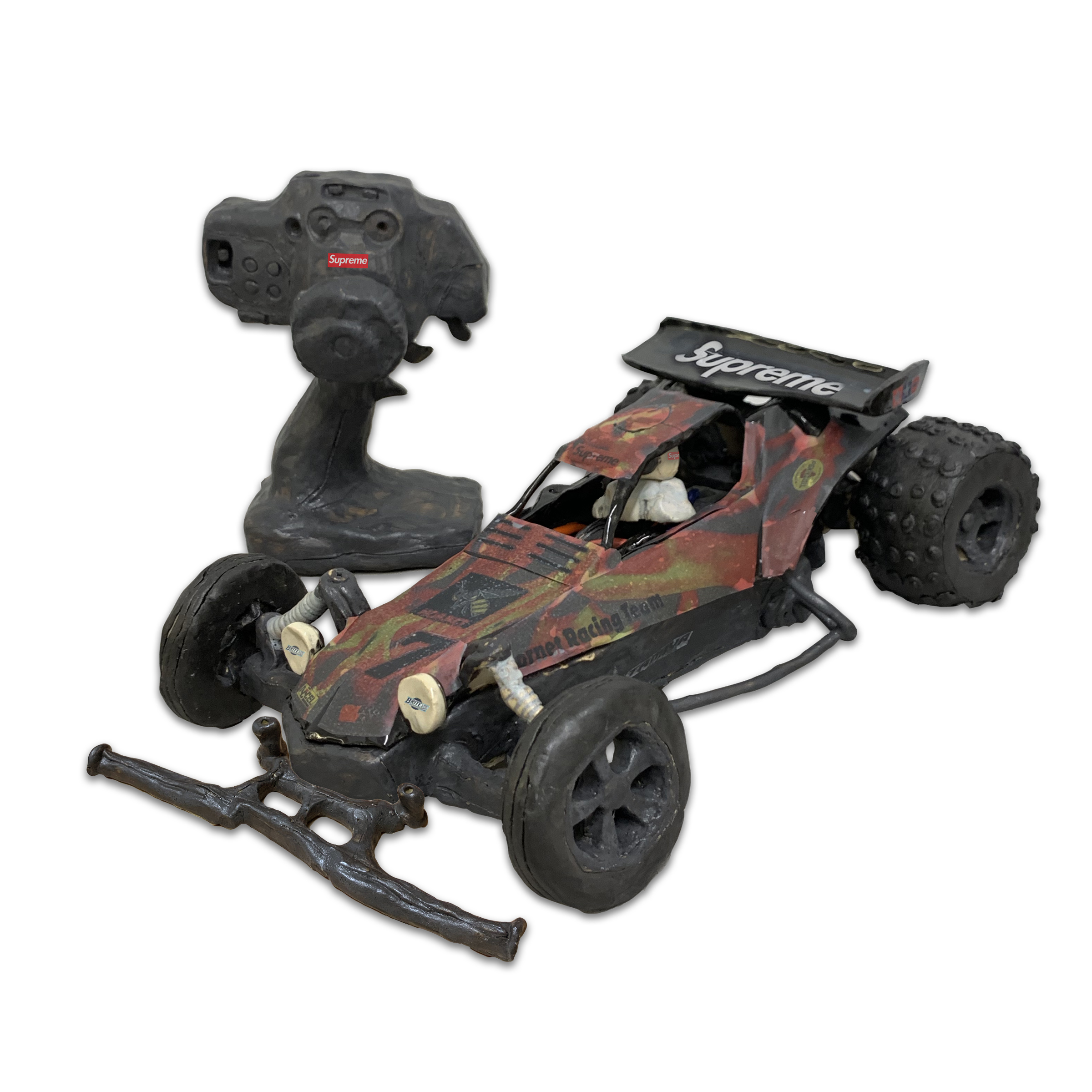 A ceramic RC car and remote control rendered in dark clay with red and gold painted detailing. The car features oversized black wheels, an open cockpit design, and a Supreme logo decal on its hood, while the controller sits beside it with its antenna extended.