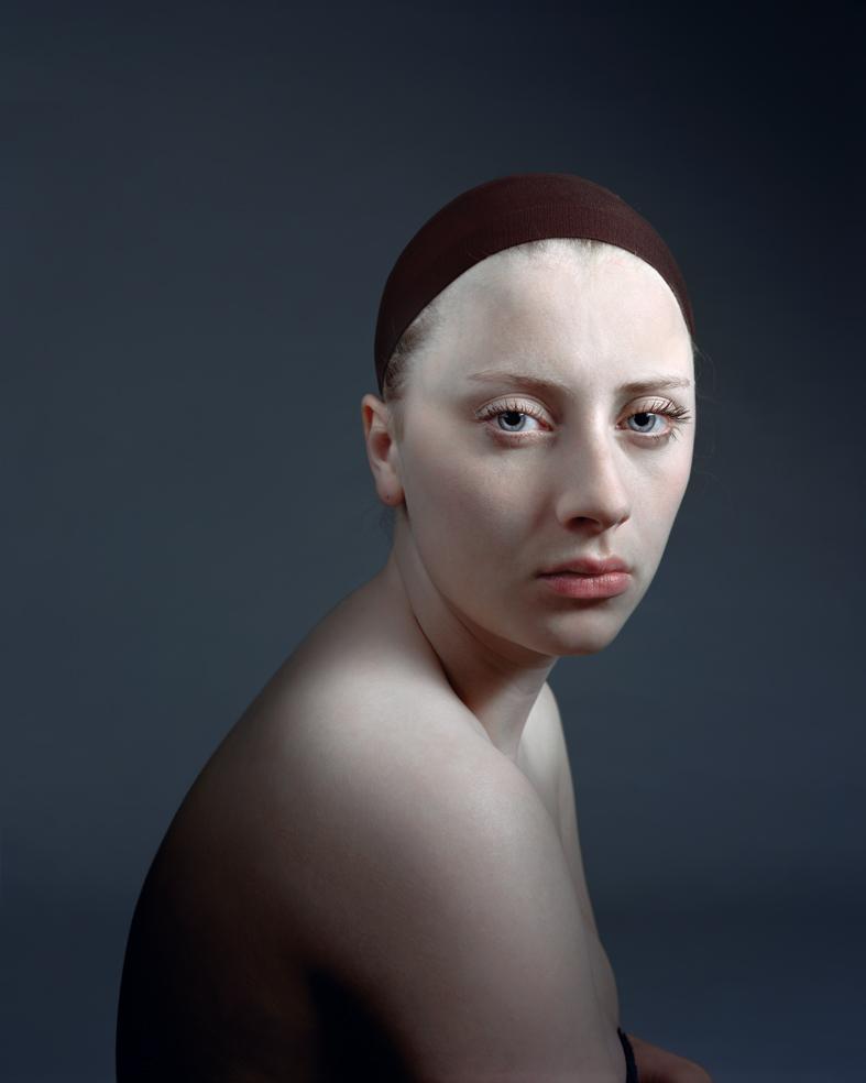 Portrait of a pale-skinned figure with shaved head wearing a dark maroon headband, shown in three-quarter view against a cool blue-gray background. The figure has a contemplative expression and bare shoulders, rendered with precise detail and smooth modeling of form.