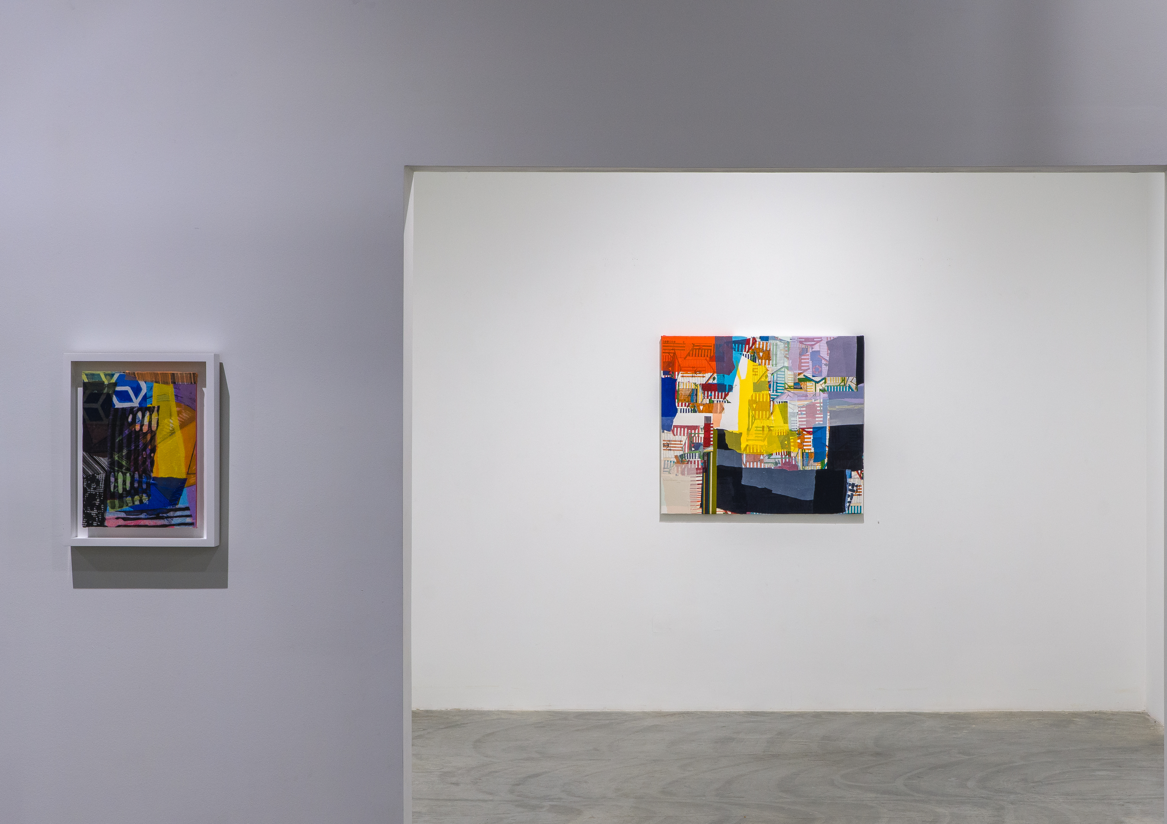 Two framed mixed-media compositions featuring layered fabrics, photographs, and paint in vibrant colors including blue, yellow, orange, and purple, hung on a white gallery wall—the smaller work on the left with darker tones and geometric shapes, the larger work on the right with bright chromatic passages and collaged elements creating visual complexity and misalignment.