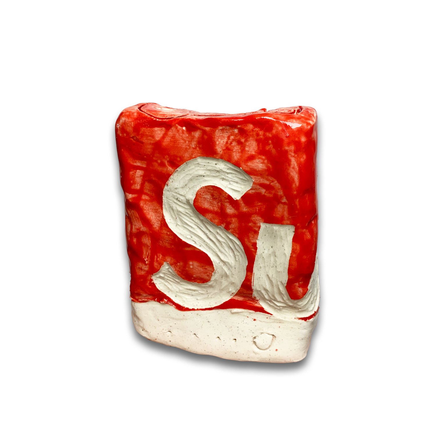 A ceramic block with a bright red glazed surface features white carved letters "SI" in the center. The piece has a cream-colored base and displays gestural, hand-applied surface treatment with visible texture and brushwork throughout.