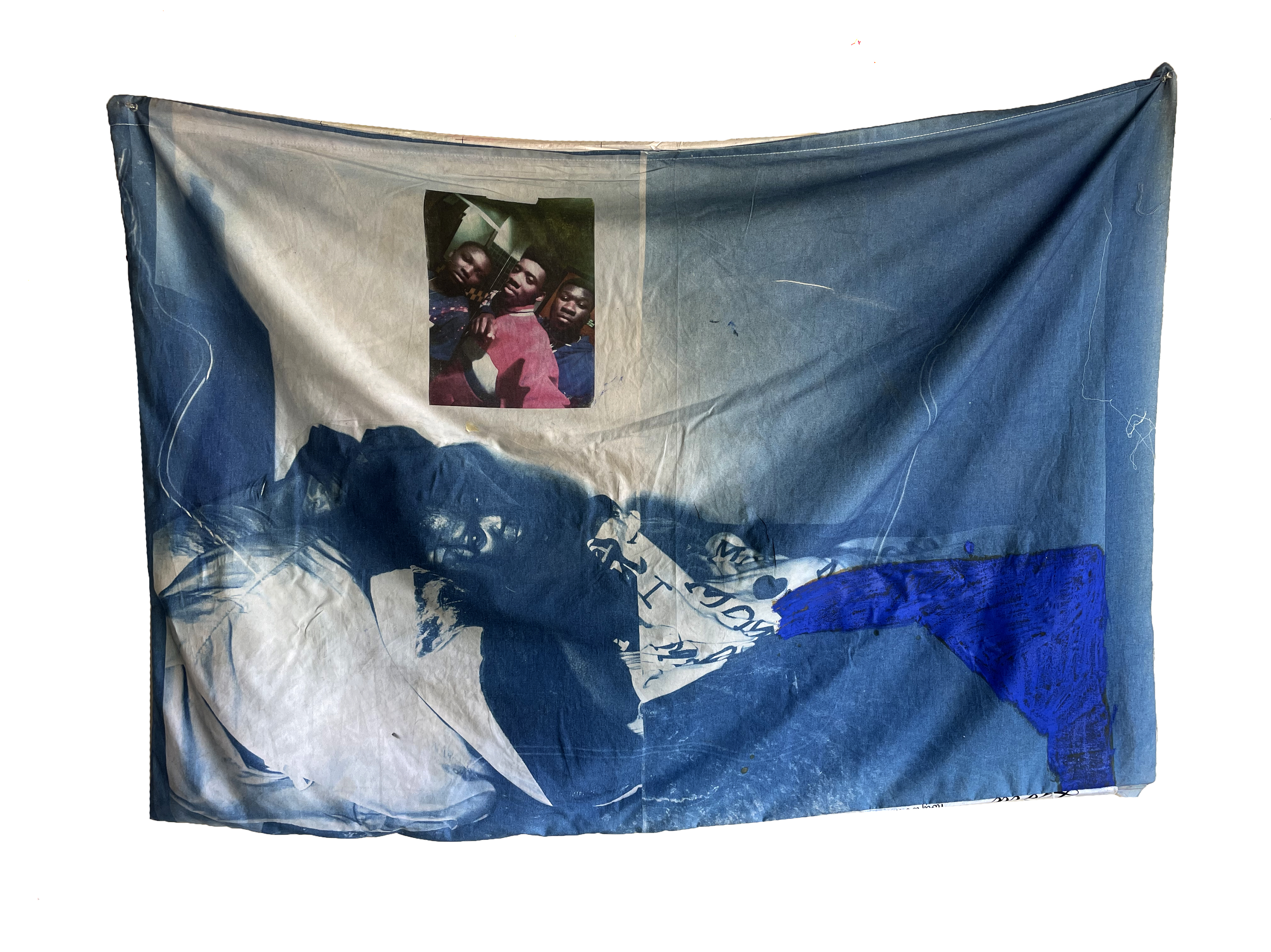 A large blue and white fabric artwork featuring cyanotype and photographic imagery of a reclining figure in the lower portion, with a smaller photograph of three smiling faces mounted in the upper center. The composition combines deep indigo and navy tones with cream-colored sections, creating a layered, atmospheric effect across the cotton textile.