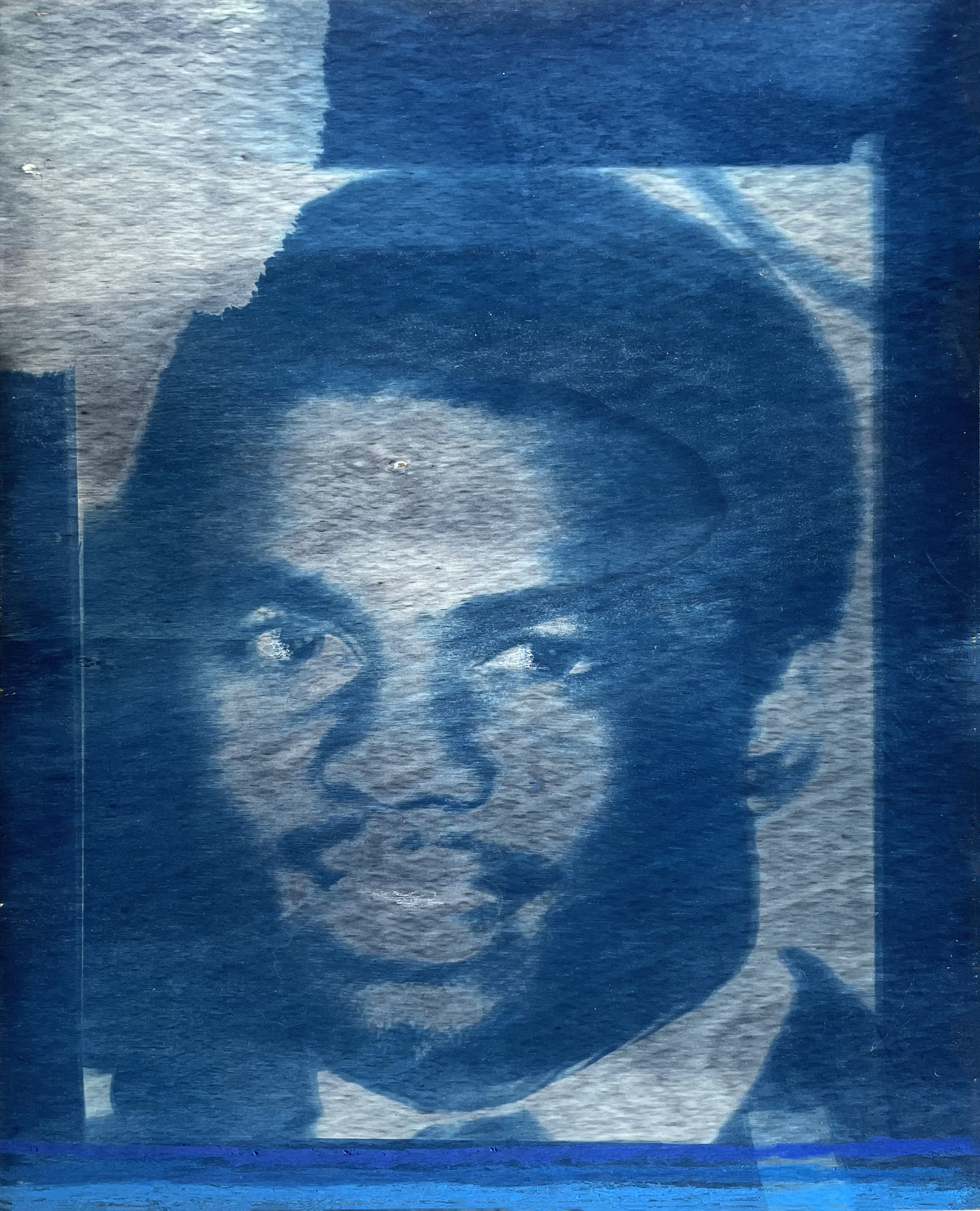 A portrait rendered in deep blue and silvery gray tones shows a person's face in profile, looking downward. The image has a luminous, ethereal quality characteristic of cyanotype printing, with soft gradations between the cool blue shadows and lighter areas that suggest form and dimensionality.