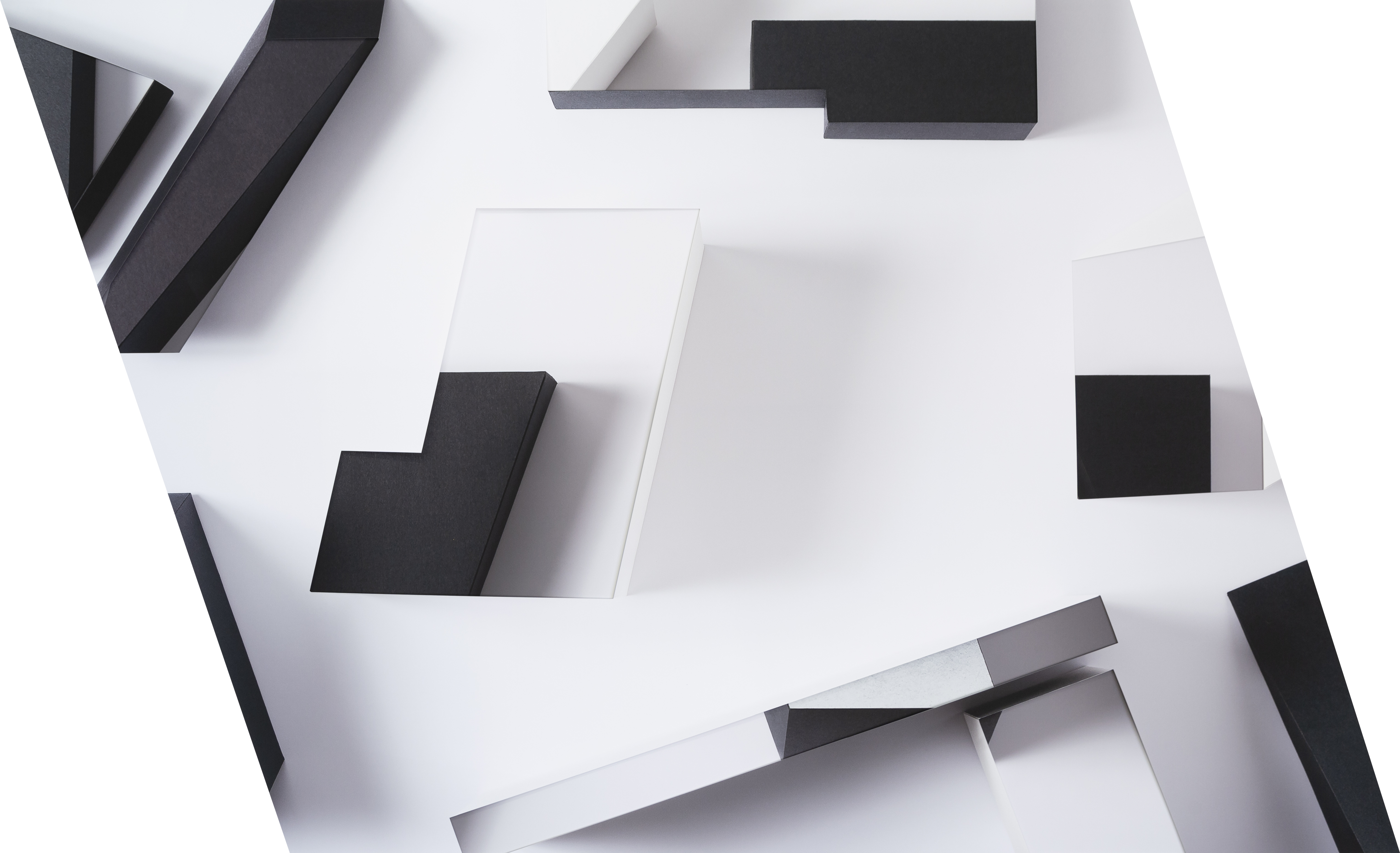 Overhead view of an abstract architectural composition featuring layered white and light gray planes intersected by bold black rectangular forms. The decollaged design creates dimensional depth through overlapping cut and folded paper elements that cast subtle shadows across the white surface.