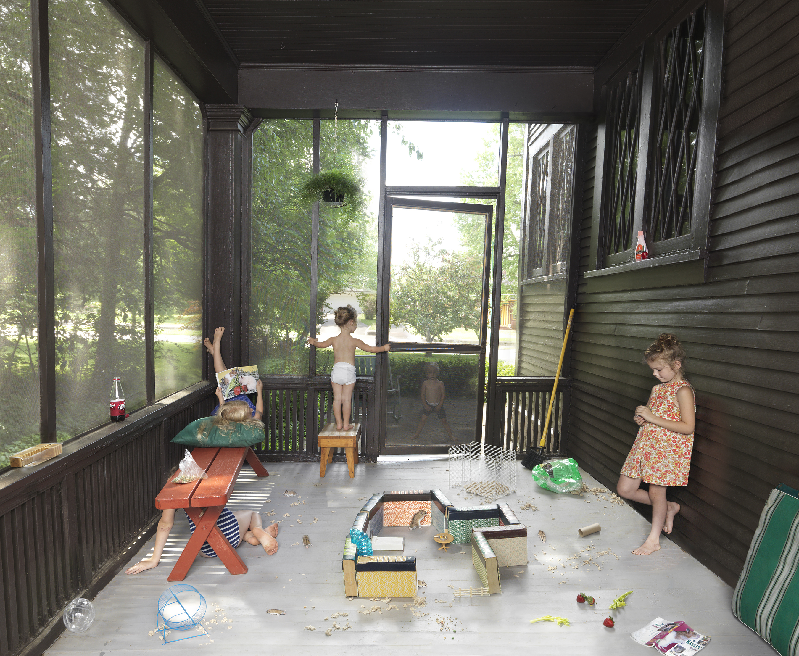 Three young children play in a screened porch filled with sand and various containers, with large windows framing green foliage outside. The scene captures a casual, playful domestic moment rendered in bright, saturated color with meticulous attention to everyday details and materials.