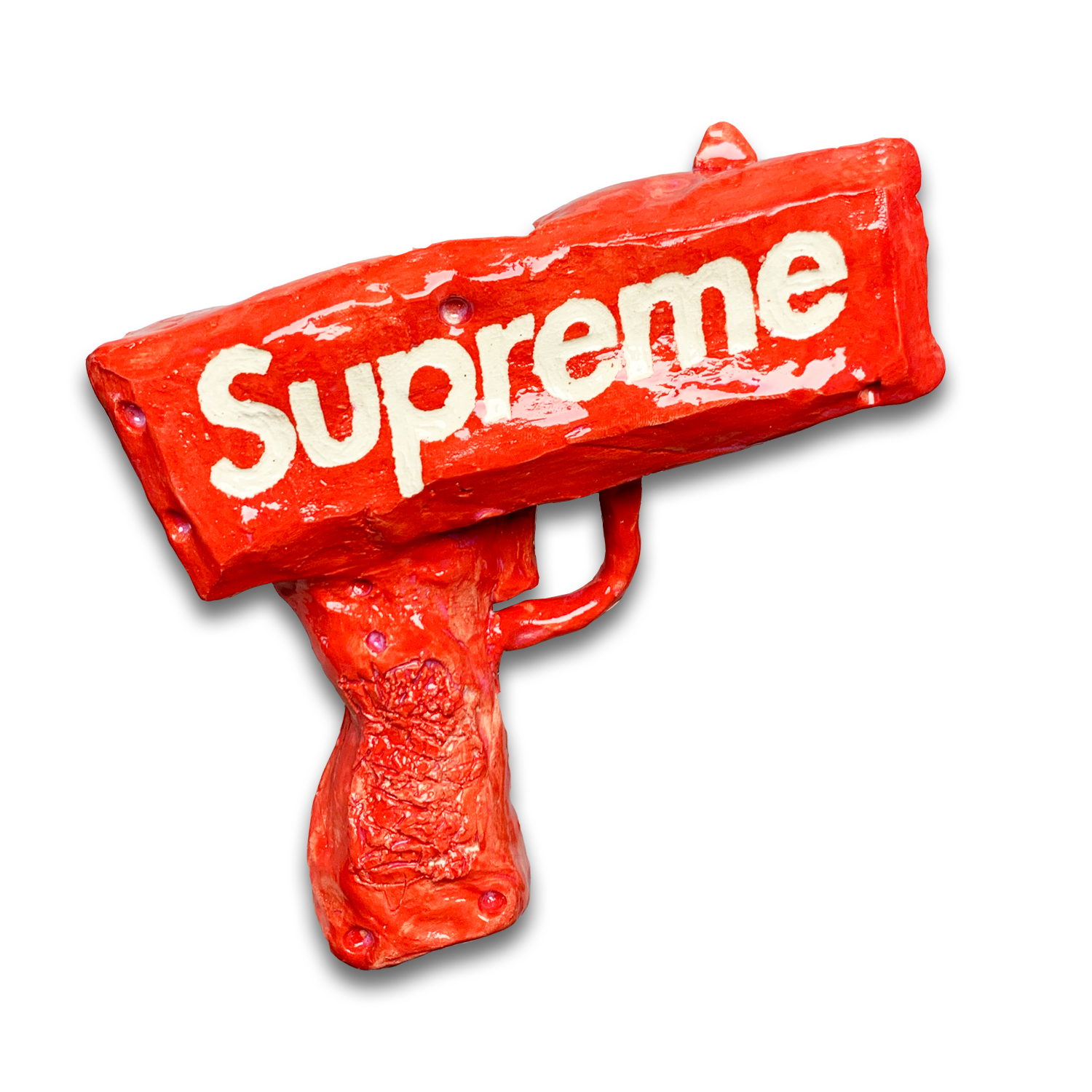 A bright red sculptural gun with white lettering spelling "Supreme" on its barrel. The figurative form is crafted from clay with a glossy glazed finish, featuring a textured grip and trigger mechanism, set against a white background.