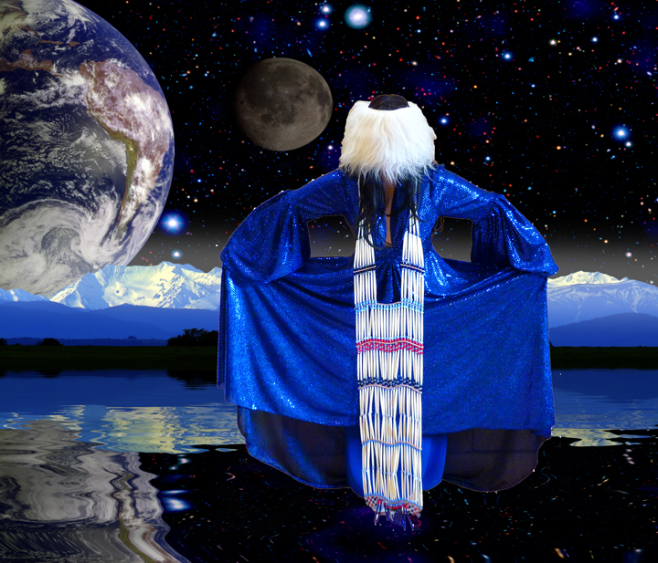 A figure with long white hair viewed from behind stands before a cosmic landscape, wearing a brilliant blue sequined cape over a white beaded garment resembling Big Ben. Earth and moon loom large in a starlit sky above snow-capped mountains reflected in still water below.