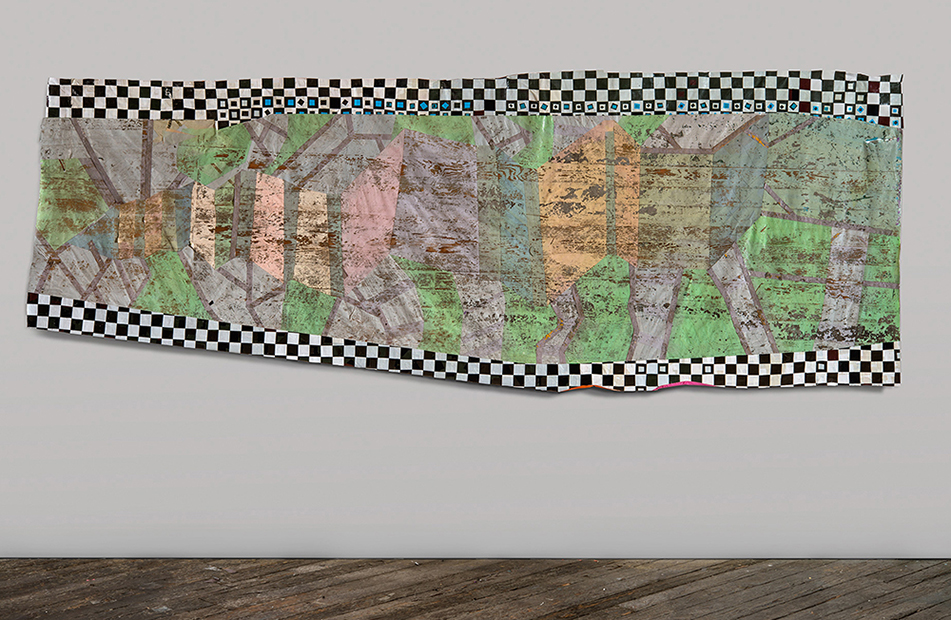 A horizontal mixed-media collage featuring layered aerial or cartographic imagery in greens, browns, and muted tones, bordered by a black and white checkered pattern. The composition is mounted on a light gray wall above wooden flooring, with the irregular edges and translucent quality of the materials creating depth and visual complexity.