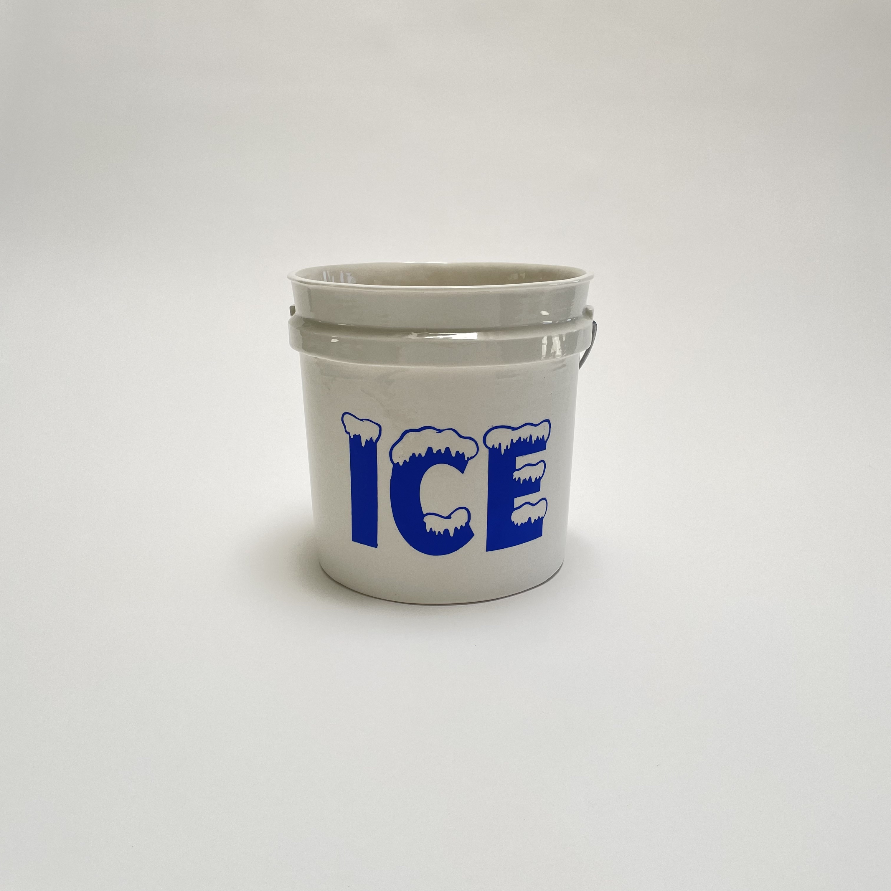 A white porcelain bucket with a metal handle features the word "ICE" in bold blue letters with textured icicle details across the top of each letter. The cylindrical form is rendered in clean, minimalist style against a neutral background.