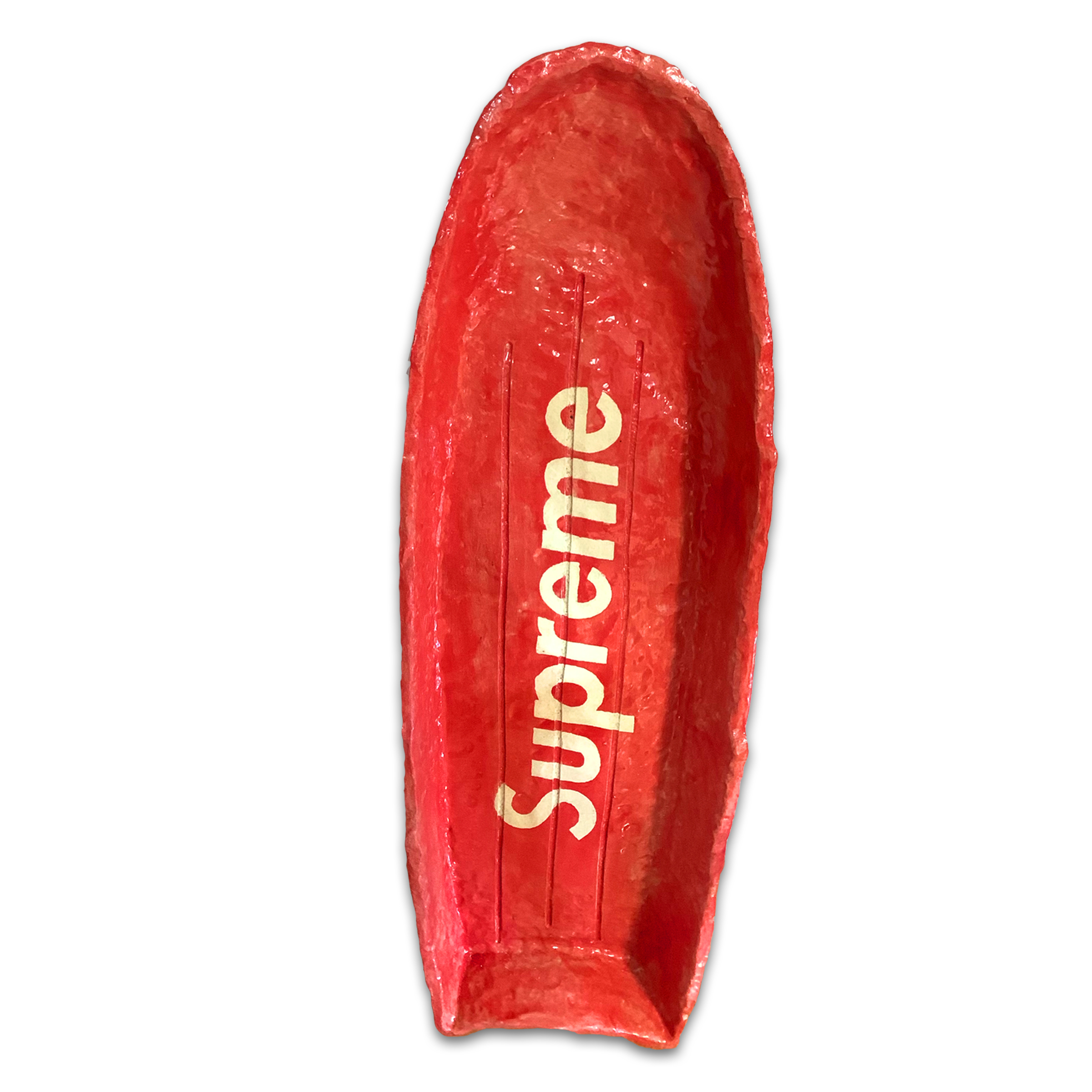 A bright red ceramic form resembling a flattened boat or sled, glazed with a glossy finish. Gold lettering reading "Supreme" runs vertically down the center of the elongated vessel, which tapers slightly at both ends and features a subtle curved rim.