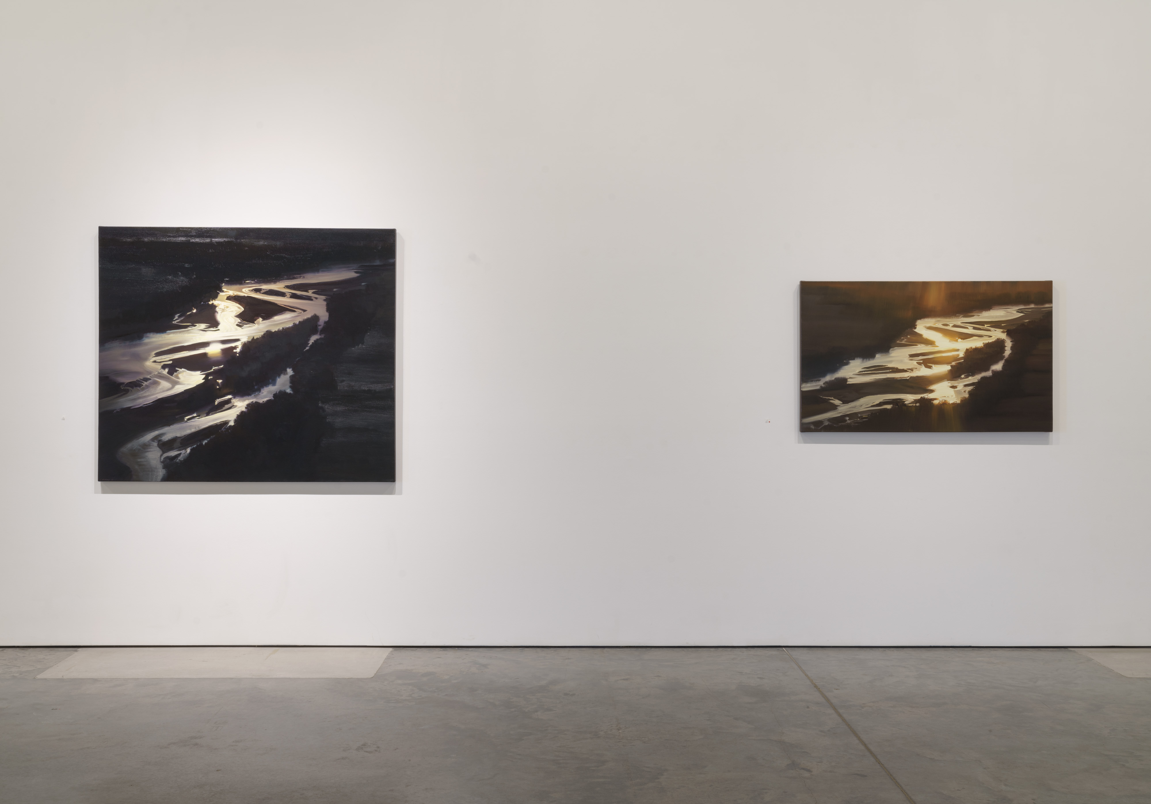 Two oil paintings mounted on a gallery wall depicting aerial views of a winding river at dusk. The larger work on the left and smaller work on the right both feature luminous curves of water rendered in cream and pale yellow tones against deep, richly textured blacks and browns, with multidirectional brushstrokes creating optical shimmer and atmospheric depth.