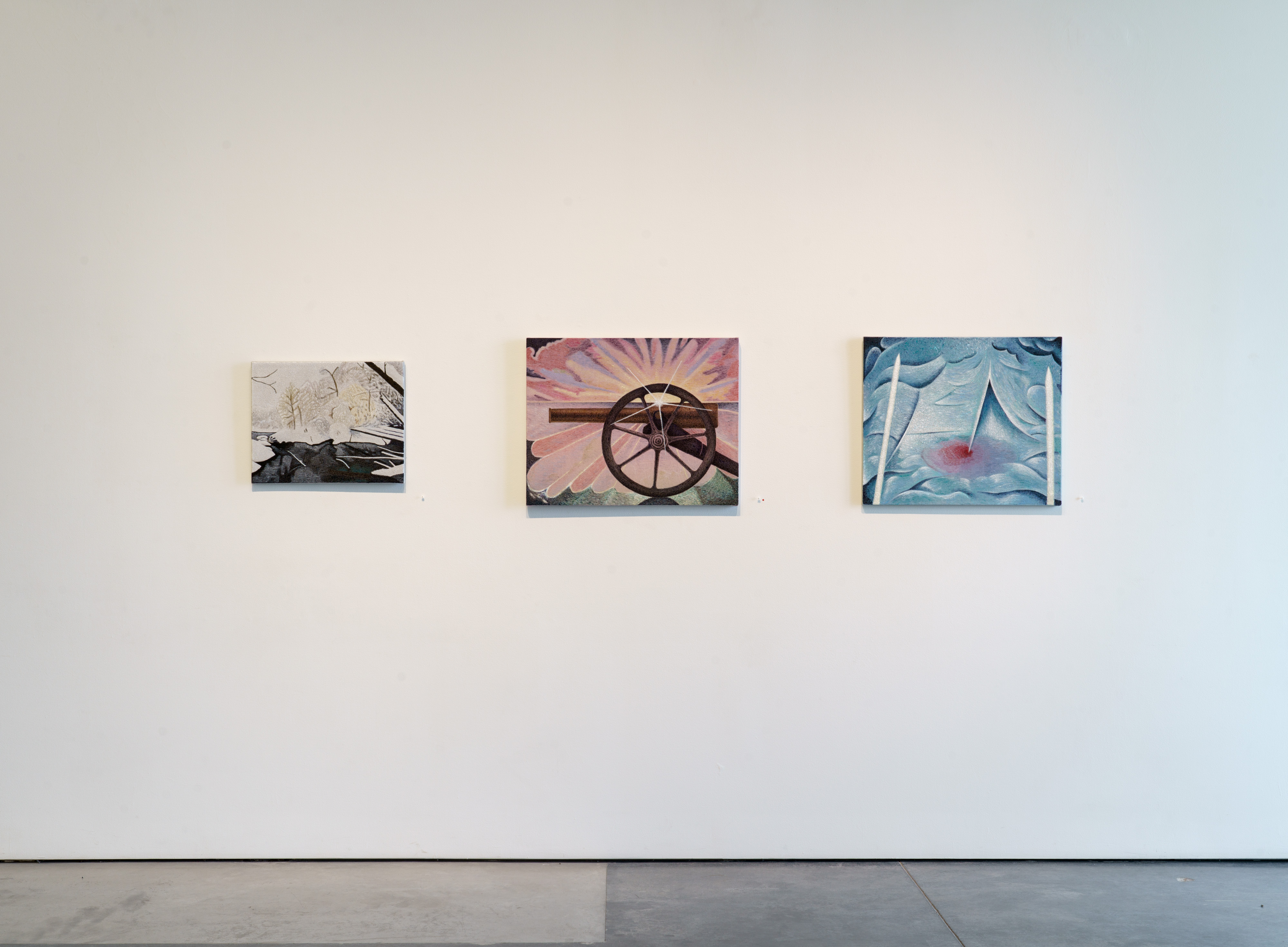 Three paintings displayed horizontally on a white gallery wall at eye level. Left canvas features black silhouettes of bare branches against a light background. Center canvas depicts a wooden wagon wheel silhouetted against a radiating pink and yellow sunburst. Right canvas shows blue-toned abstract forms with curved shapes and a red accent. Each work is mounted individually with subtle shadows cast on the wall below.