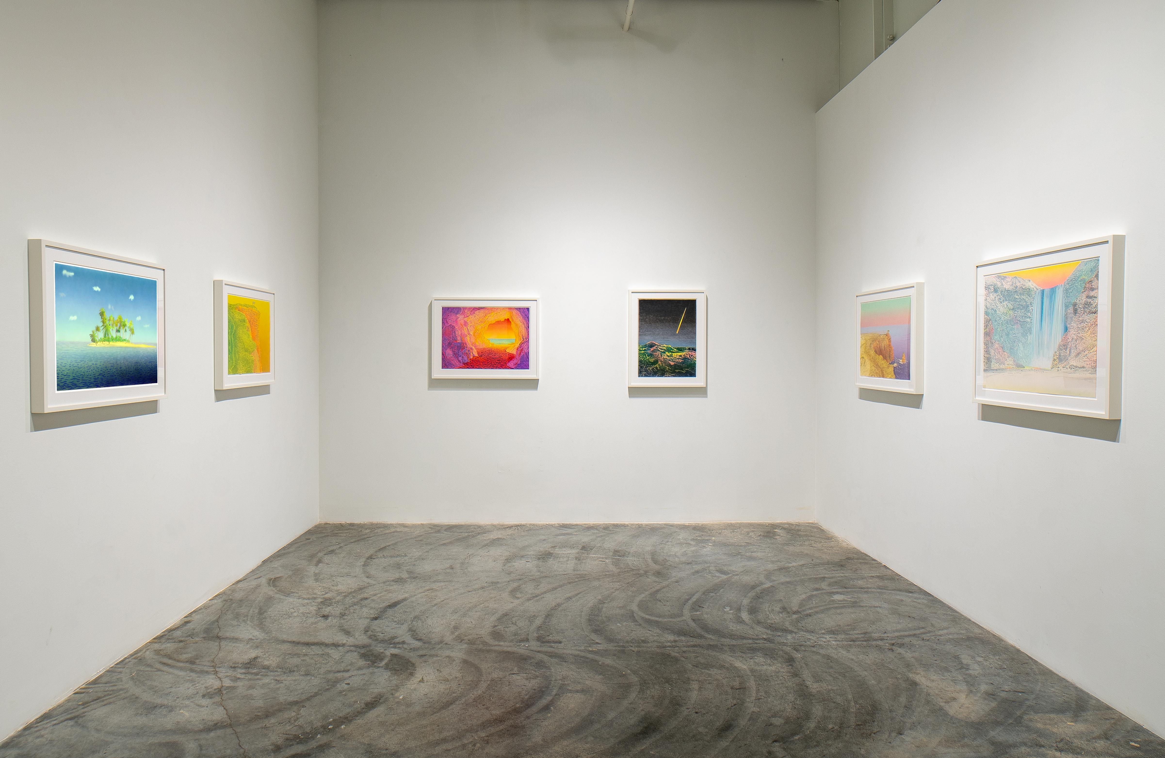 White gallery walls display six framed artworks arranged across three walls. The works feature vibrant landscapes and abstract compositions in varied color palettes—rich yellows and oranges, purples and reds, cool blues and greens—rendered in painterly styles. Concrete flooring grounds the minimalist exhibition space, with soft gallery lighting casting subtle shadows on the white walls.