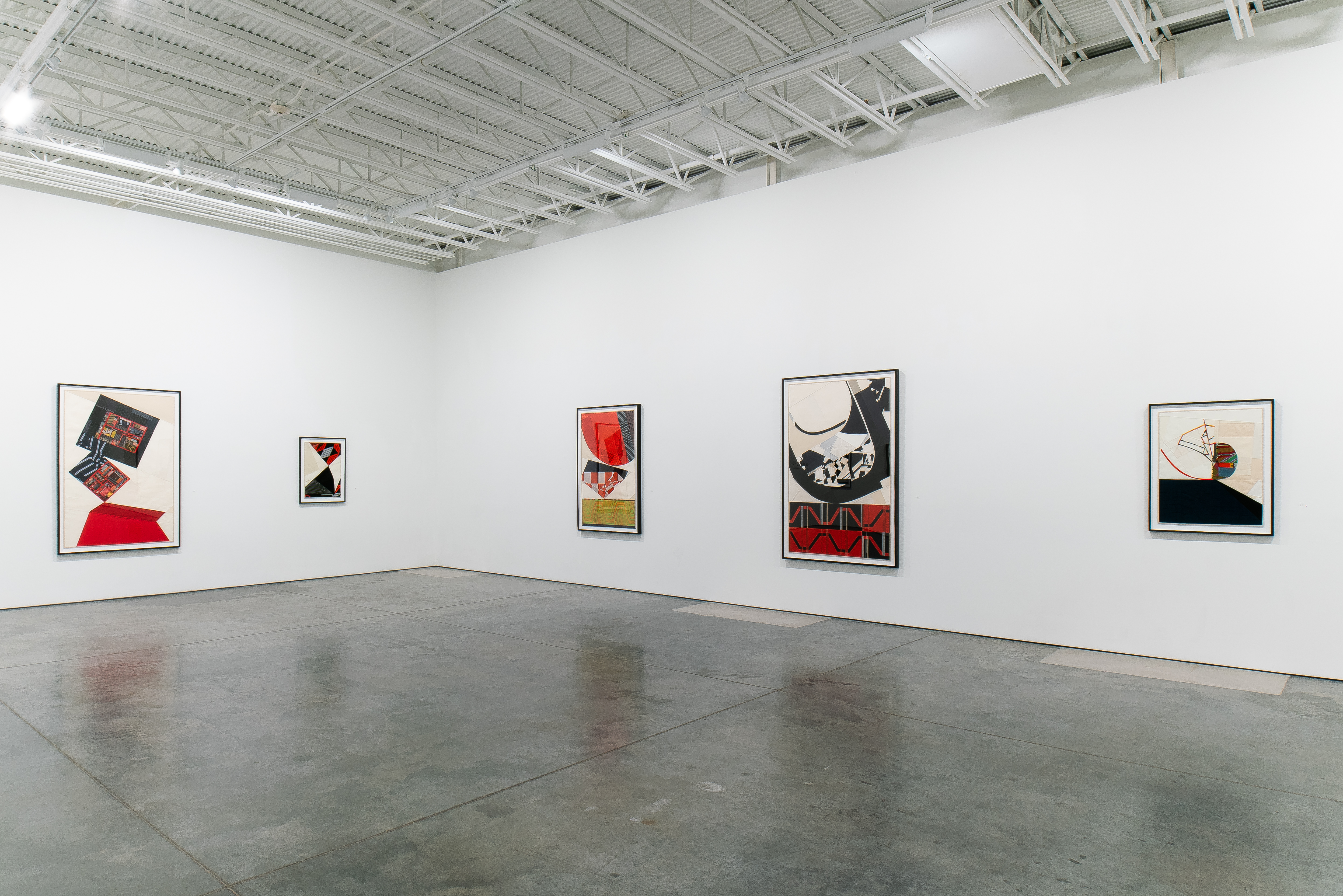 Five framed abstract textile collages hang on white gallery walls, each featuring vivid compositions of layered vintage fabrics in bold geometric patterns. The works incorporate vibrant reds, blacks, creams, and earth tones, with dynamic arrangements of cut and pieced materials creating a sense of controlled chaos and movement across neutral backgrounds.