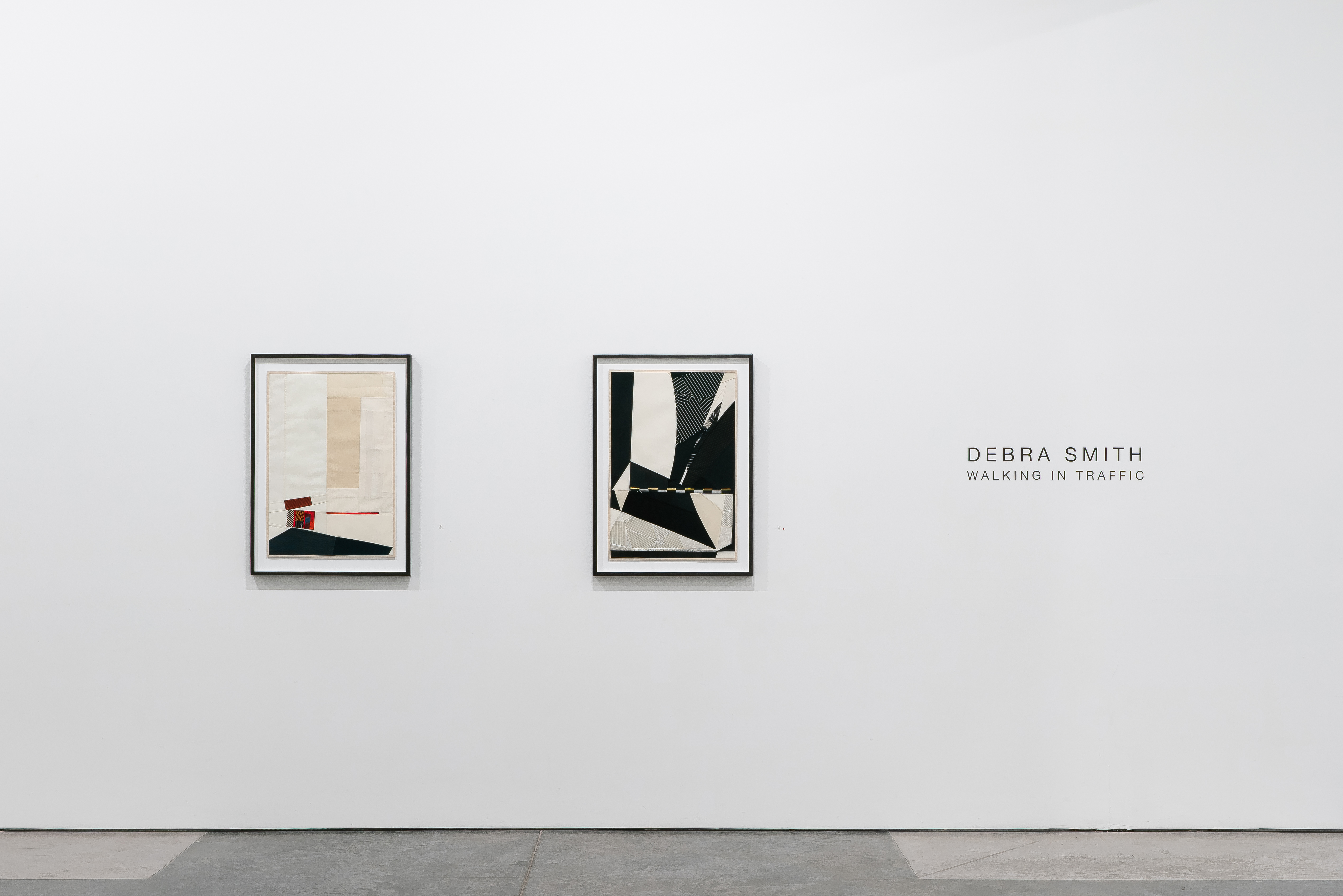 Two framed abstract textile collages hang on a white gallery wall. The left work features muted beige and cream tones with a small red rectangular element and dark navy shape. The right work displays bold black and white geometric forms with diagonal lines and contrasting shapes. Both pieces demonstrate layered fabric composition with controlled color blocking and modernist abstraction.