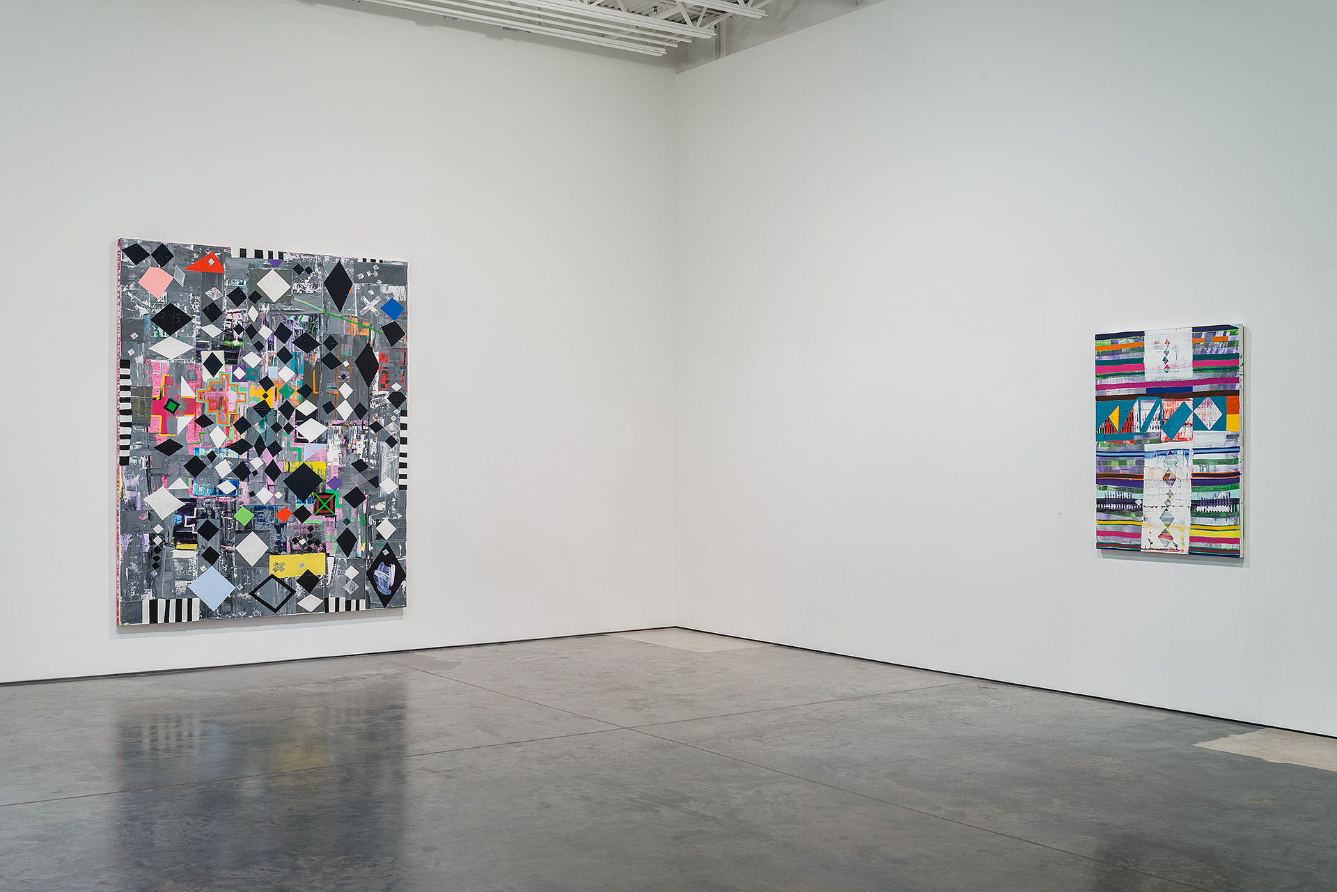 Two large abstract paintings hang on white gallery walls. The left work features a dense composition of black, white, and colored diamond shapes layered over photographic and textural elements, bordered by striped patterns. The right work displays horizontal bands of vibrant colors including rainbow hues, interspersed with white sections containing geometric patterns and line drawings.