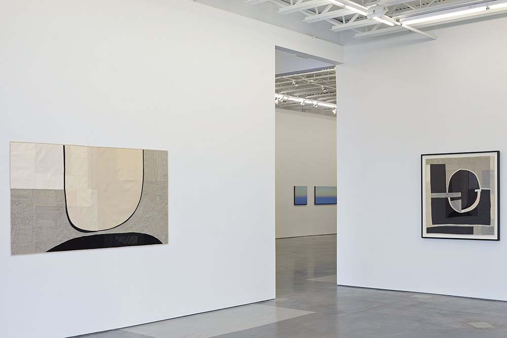 Contemporary abstract textile composition featuring layered fabric in cream, black, and striped patterns arranged with bold gestural curves and geometric forms. Two additional framed textile works visible in adjacent gallery spaces, demonstrating monochromatic color palettes and minimalist graphic design across the exhibition.