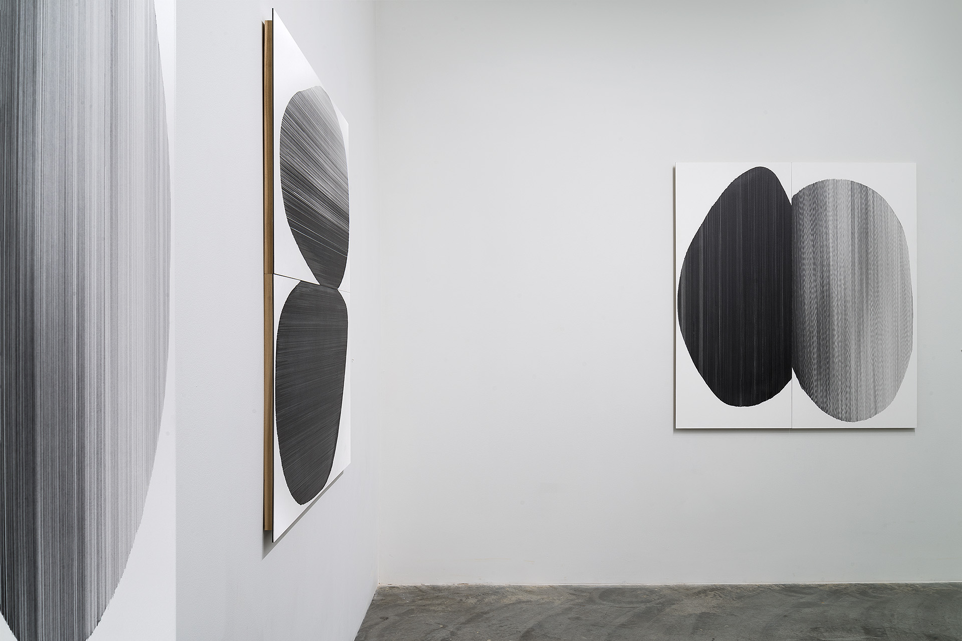 Two framed works on a white gallery wall featuring pairs of dark, hand-drawn oval forms rendered in black on white paper with textured, linear surfaces. The left drawing displays a single vertical pair; the right work shows two pairs arranged side by side. Both pieces emphasize high contrast and the visible intensity of hand-drawn mark-making embedded into mat board.