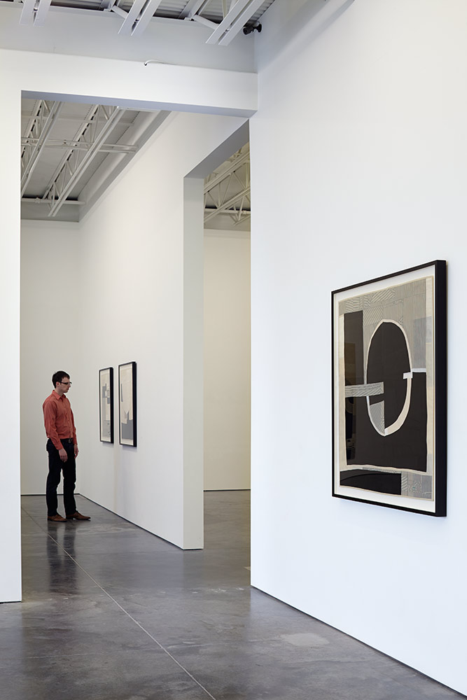 Abstract textile composition featuring bold black and white gestural forms created from pieced vintage kimono fabric and silk lining, mounted in a black frame on a white gallery wall. The work displays layered fabric creating translucent effects with organic curved shapes and graphic seams visible across the cream background.