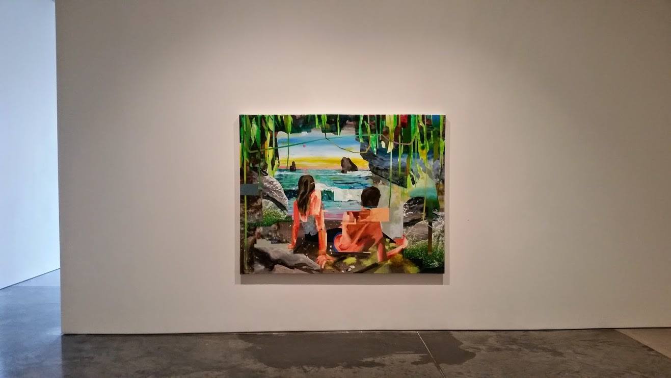 Framed digital artwork mounted on a gallery wall depicting two figures in bright orange clothing seated on rocks, gazing toward a tropical seascape framed by lush green vegetation. The composition features layered imagery with a painted landscape visible through an archway of foliage, rendered in vibrant colors including turquoise waters, golden sky, and verdant greens.