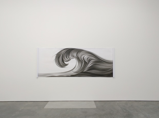 Horizontal charcoal drawing depicting a flowing wave form rendered in black and grey tones against a white background, mounted on a gallery wall. The composition shows intricate linear details creating a sense of movement and fluidity across the rectangular composition.