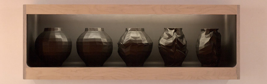 Five dark ceramic vessels arranged in a wooden shelf, progressing from rounded spherical forms on the left to increasingly angular and faceted shapes on the right, displayed against a neutral gray backdrop.
