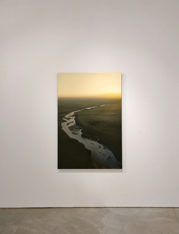Aerial photograph of a meandering river with sinuous curves cutting through dark landscape, captured at dusk with golden light reflecting off the water against a pale sky.