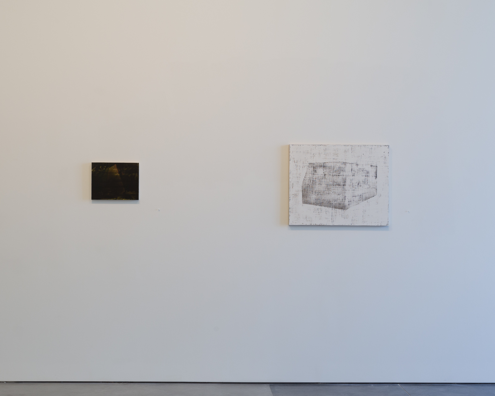 Two small framed works hang on a white gallery wall: a dark, nearly black rectangular piece on the left, and a larger white panel on the right featuring a geometric, architectural form rendered in gray linear marks and crosshatching.